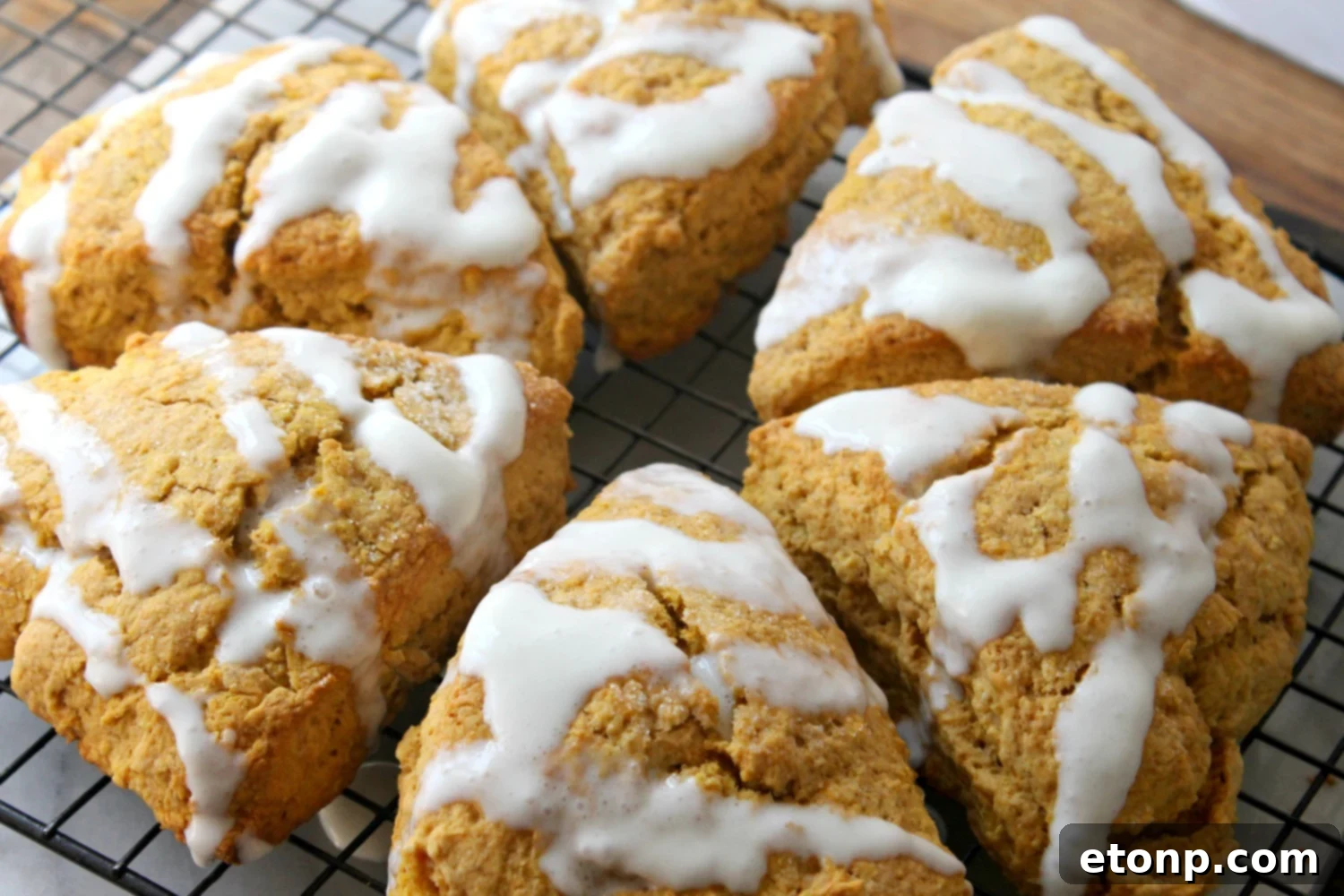 Two freshly glazed pumpkin scones on a white plate, one with extra glaze, showcasing their sweet appeal.