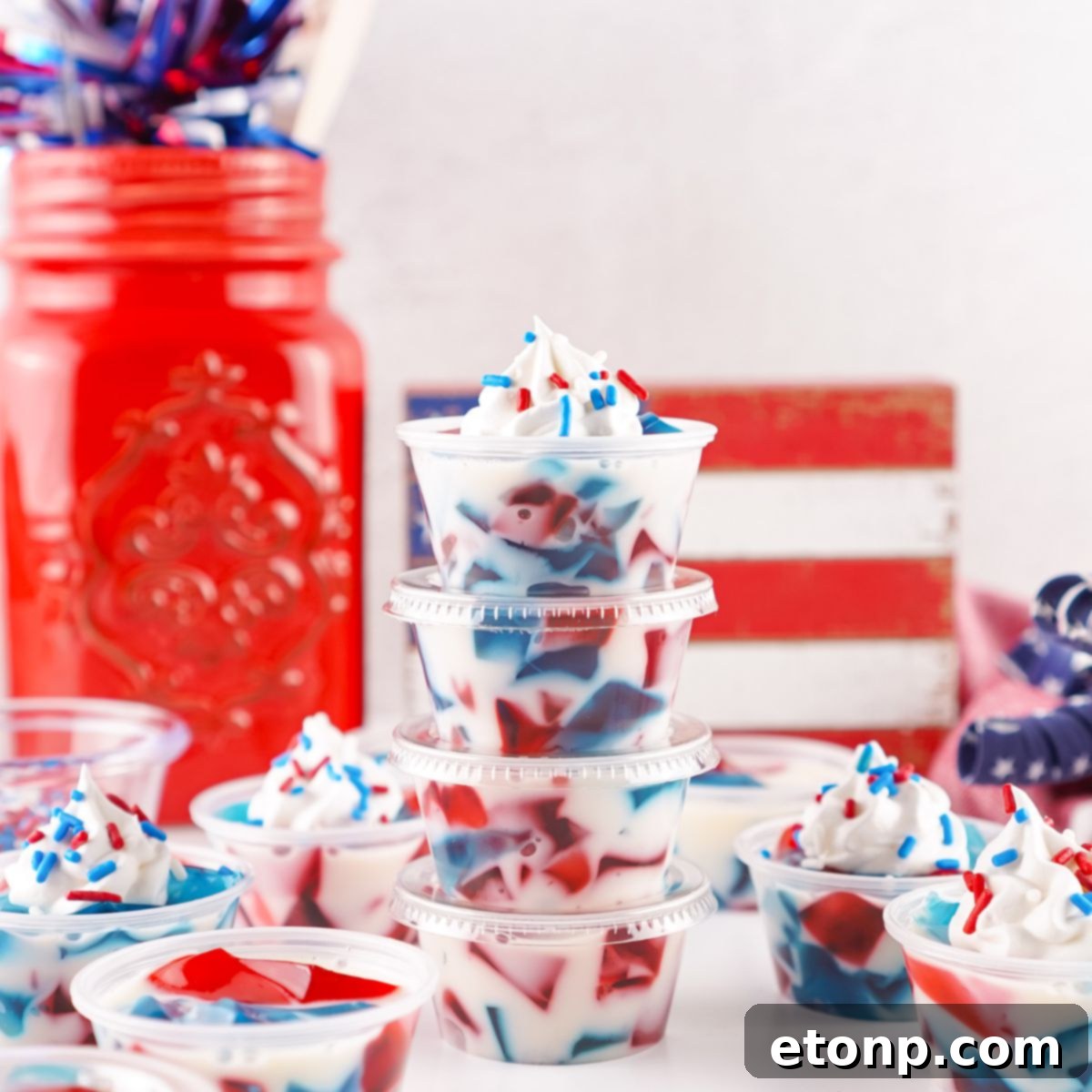 Vibrant Red, White, and Blue Stained Glass Jello Shots arranged on a table with festive patriotic decorations in the background, ready for a Fourth of July celebration.