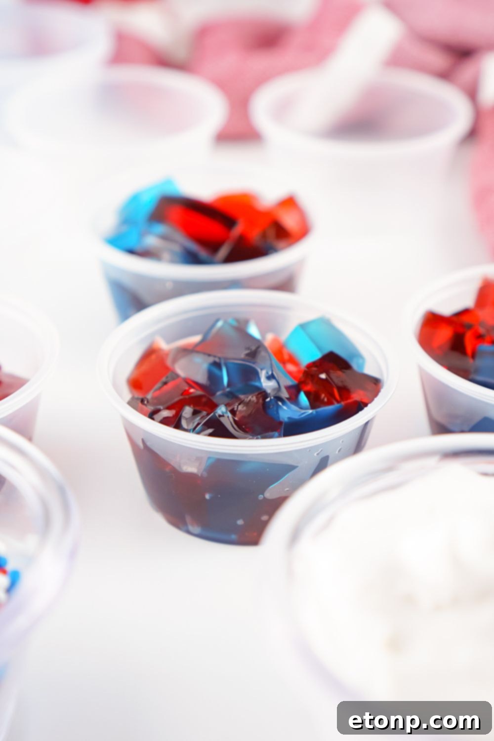 Cubed red and blue jello pieces carefully placed inside individual jello shot containers, forming the base of the patriotic treat.