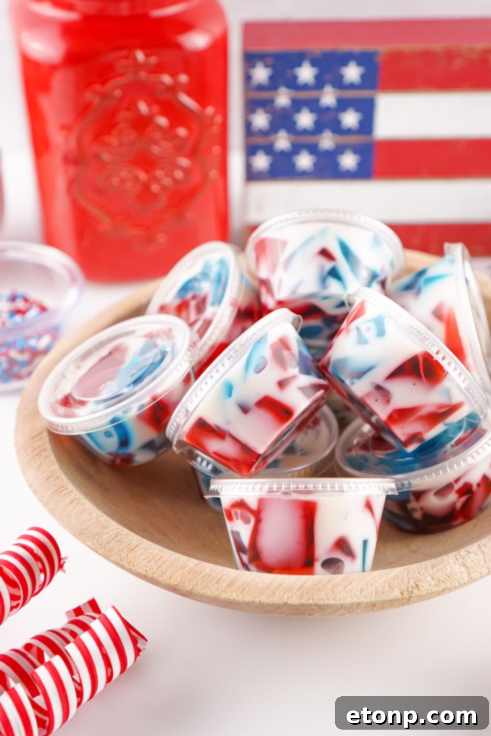 Red, White, and Blue Jello Shots displayed in a bowl on a table with a subtle American flag in the background, ready for a patriotic occasion.