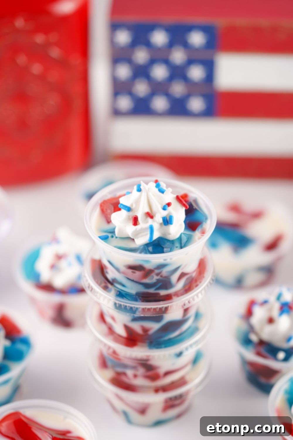 A close-up of a Red, White, and Blue Jello Shot, stacked on top of others, with whipped cream and patriotic sprinkles on top.