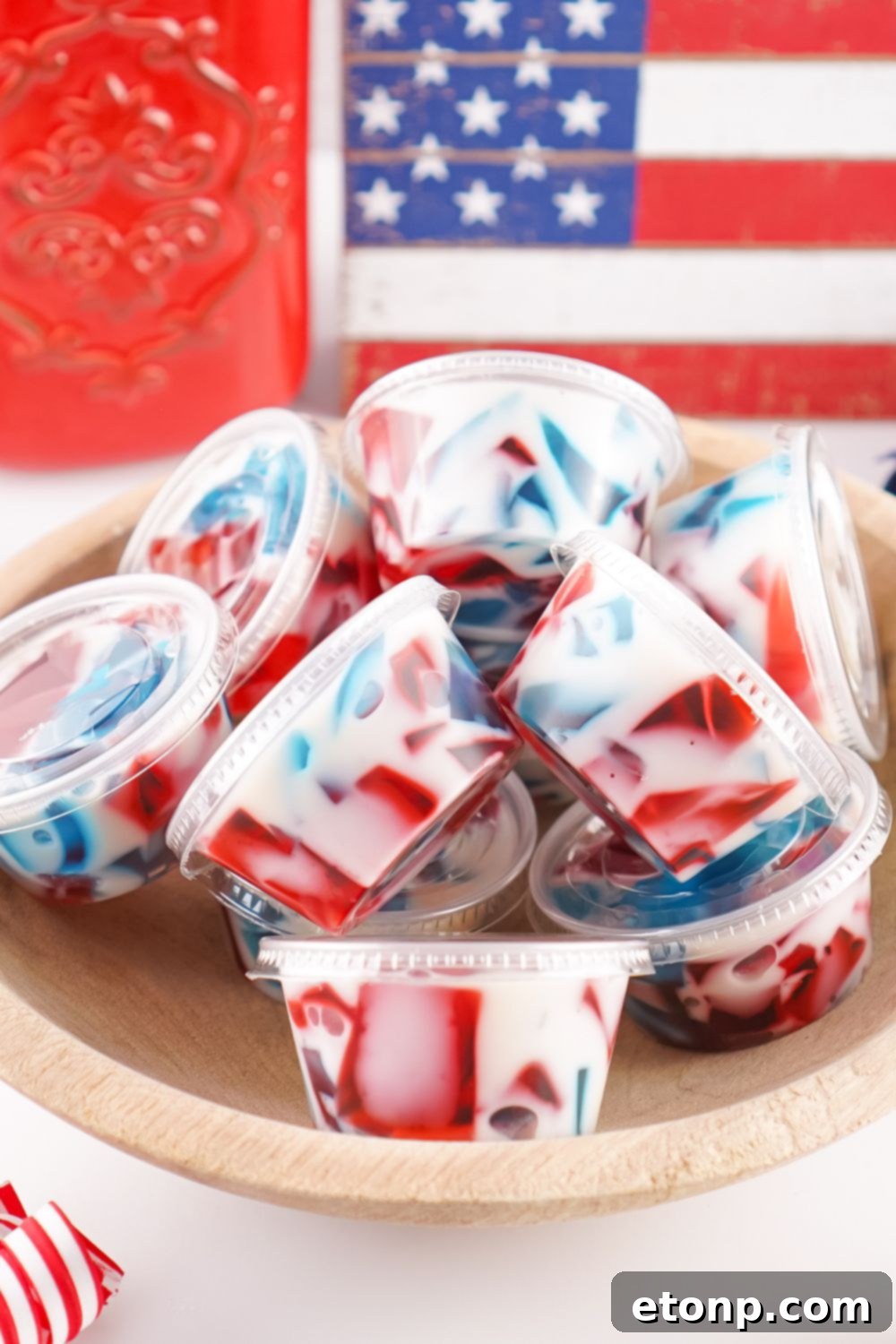 Close-up of individual Red, White, and Blue Jello Shots in small plastic containers with lids, neatly arranged in serving bowls, highlighting their layered stained glass effect.