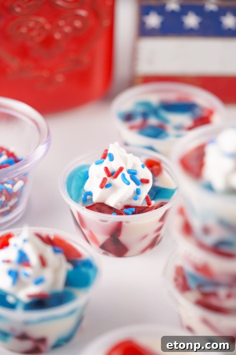 A close-up of a Red, White, and Blue Jello Shot topped with generous whipped cream and colorful red and blue sprinkles, ready to be served.