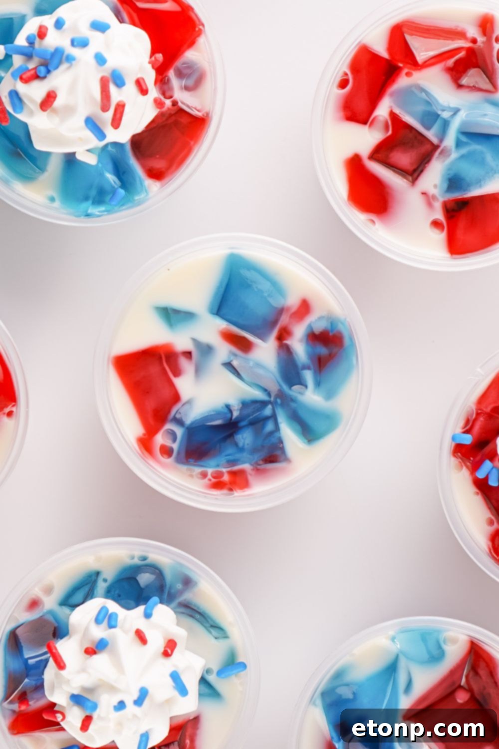 Red, White, and Blue Stained Glass Jello Shots, some topped with whipped cream and patriotic sprinkles, displayed on a table for a festive party.