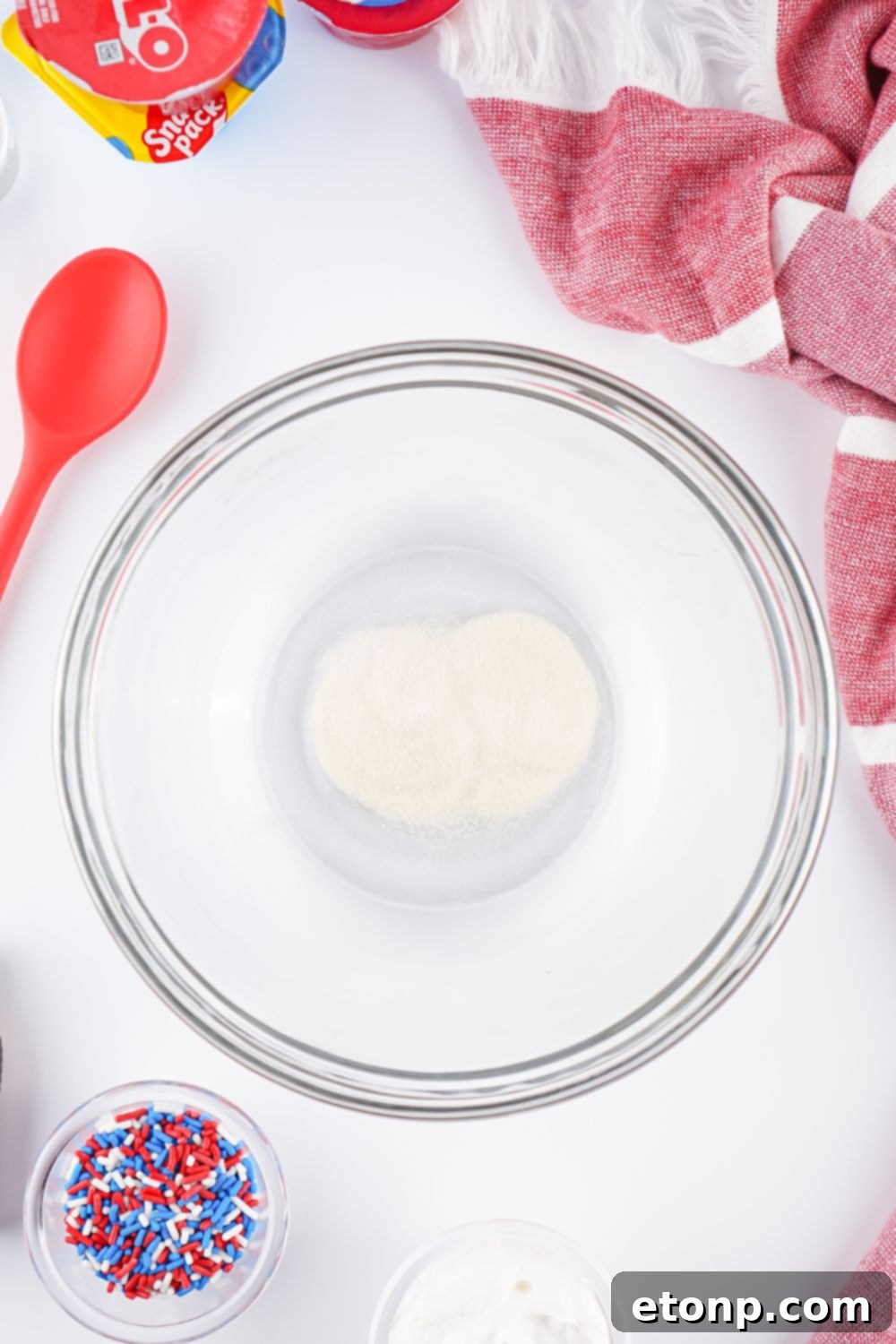 Unflavored gelatin in a glass bowl, surrounded by ingredients for Red White and Blue Jello Shots, ready for preparation.