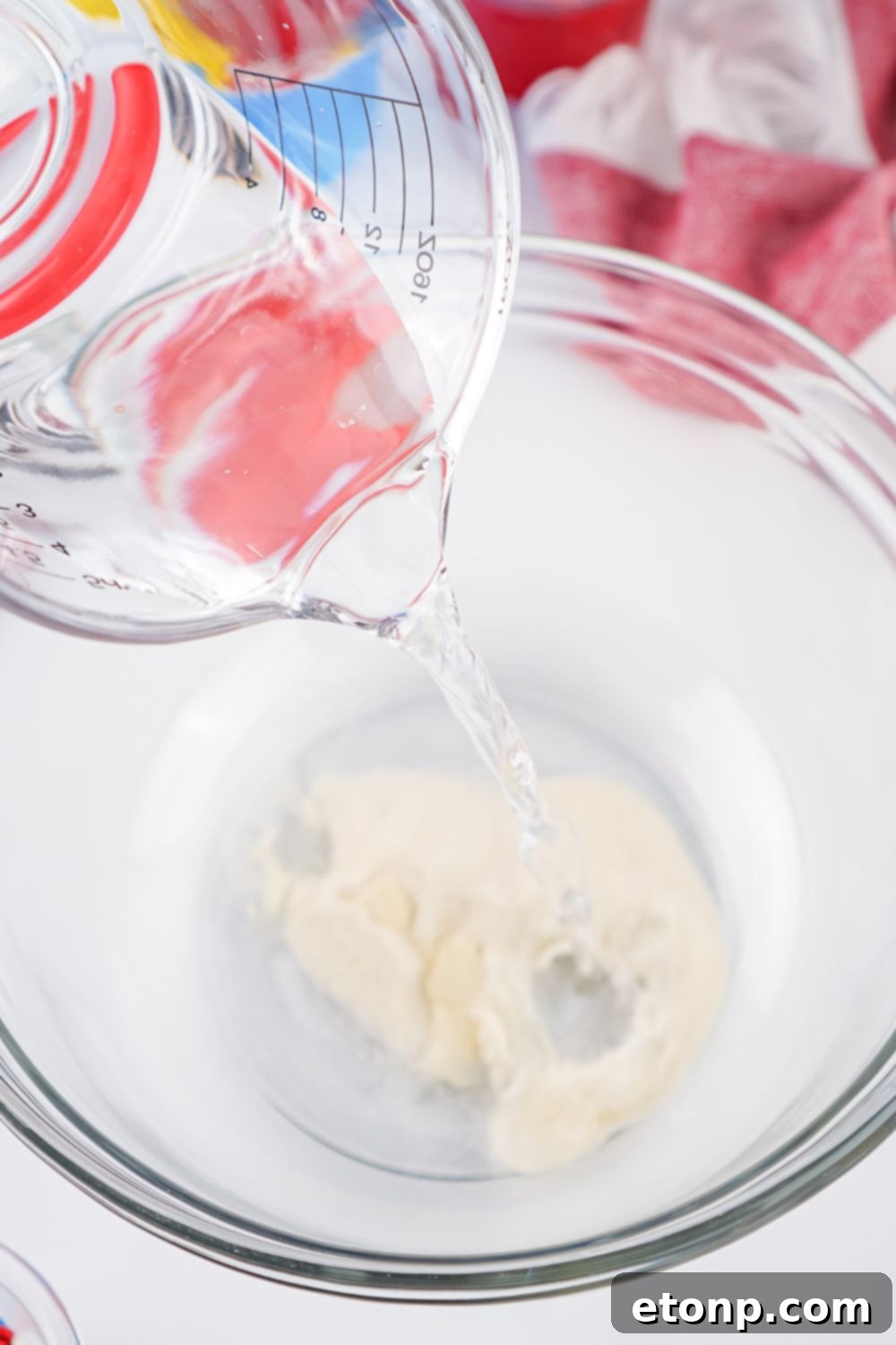 Cold water being poured over unflavored gelatin in a bowl, showing the blooming process for the jello shot recipe.
