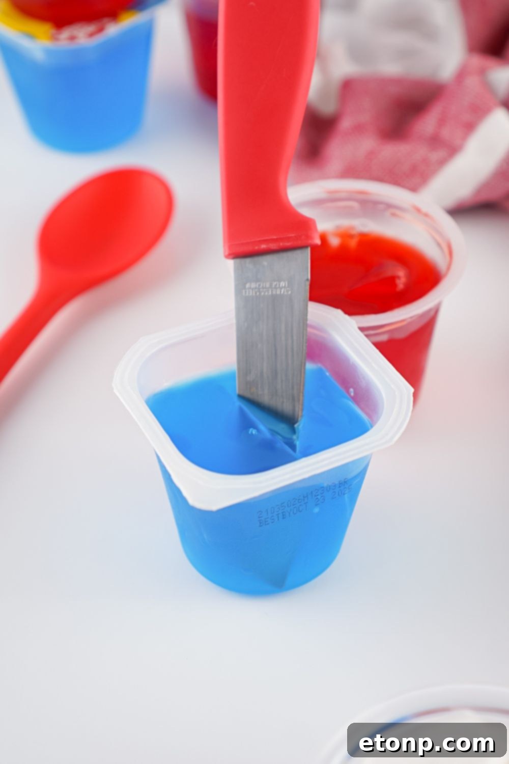 A knife slicing through a red jello cup to create small cubes, a key step for the stained glass jello effect.