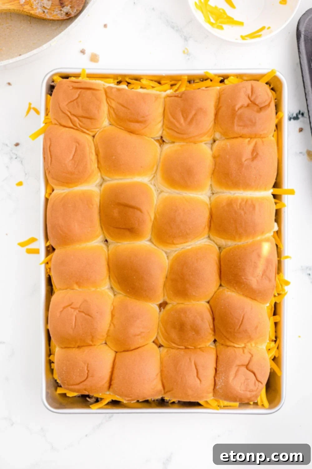 An inviting overhead shot of freshly assembled Classic Cheeseburger Sliders arranged snugly in a casserole pan, their top buns glistening, ready for their final bake.