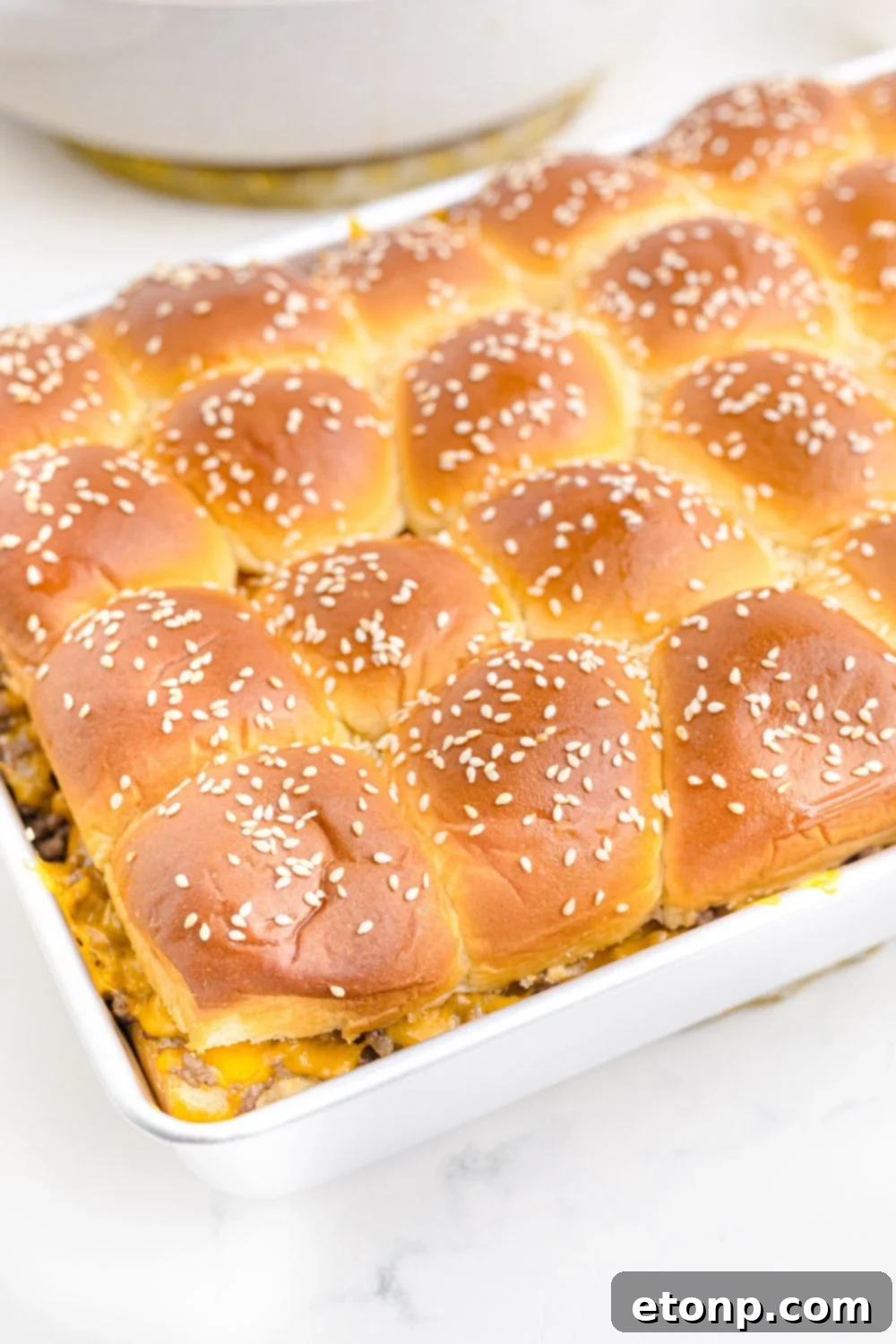 A delectable side view of Classic Cheeseburger Sliders, neatly lined up in a baking pan, showing the golden-brown buns and hints of melted cheese, promising a savory treat.