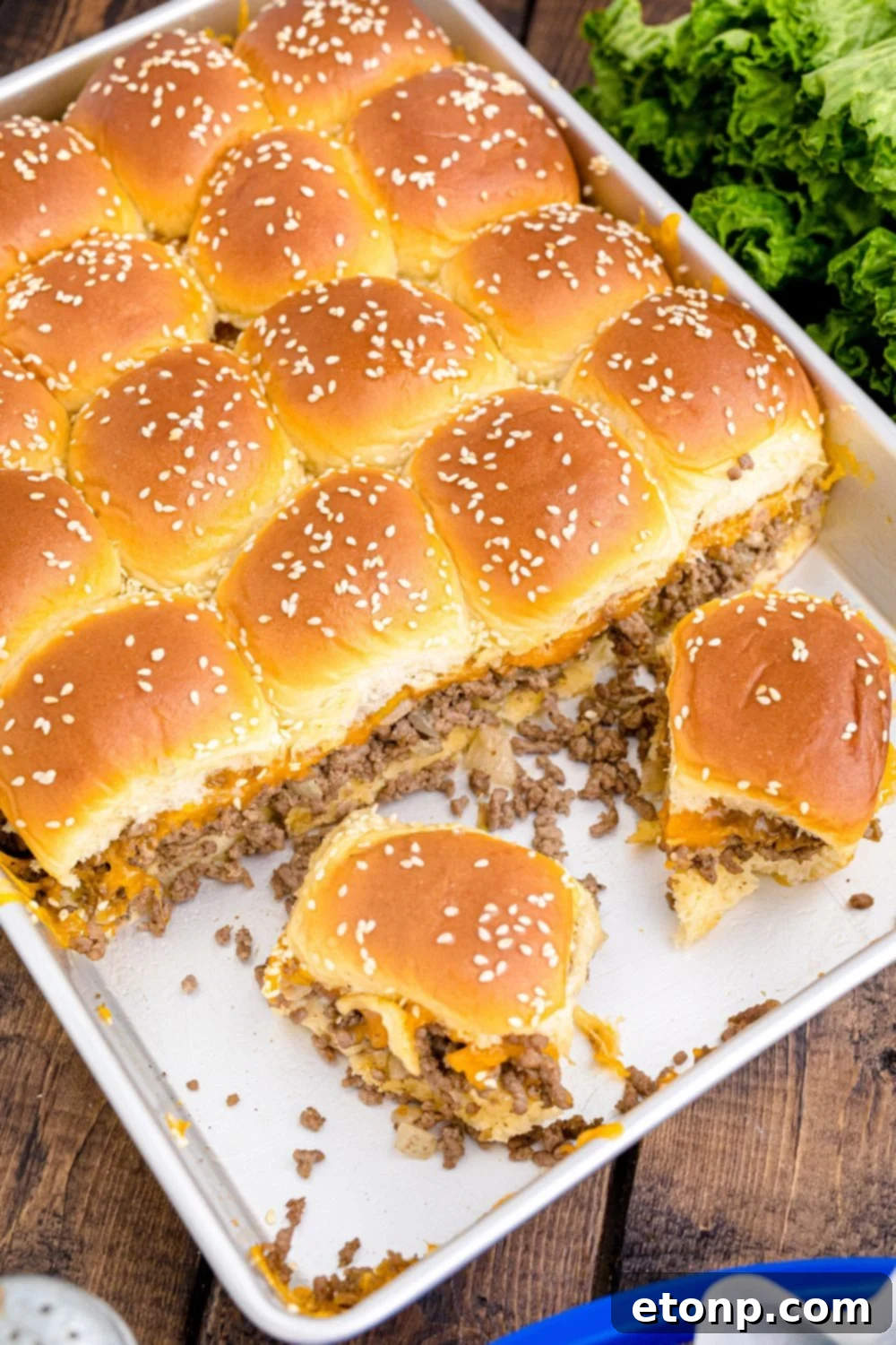 A full casserole dish of freshly baked Classic Cheeseburger Sliders, with a few already happily claimed, illustrating their popularity and inviting presentation.