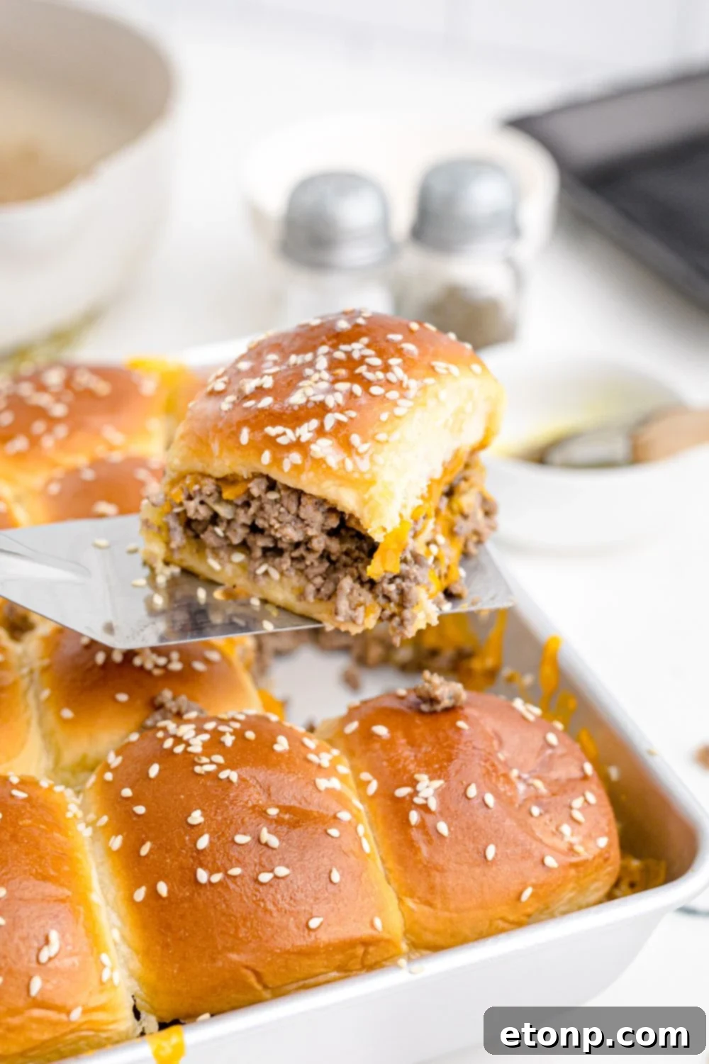 A baking pan filled with golden-brown beef and cheese sliders, with one slider being carefully lifted out, highlighting its fluffy bun and melted cheese.
