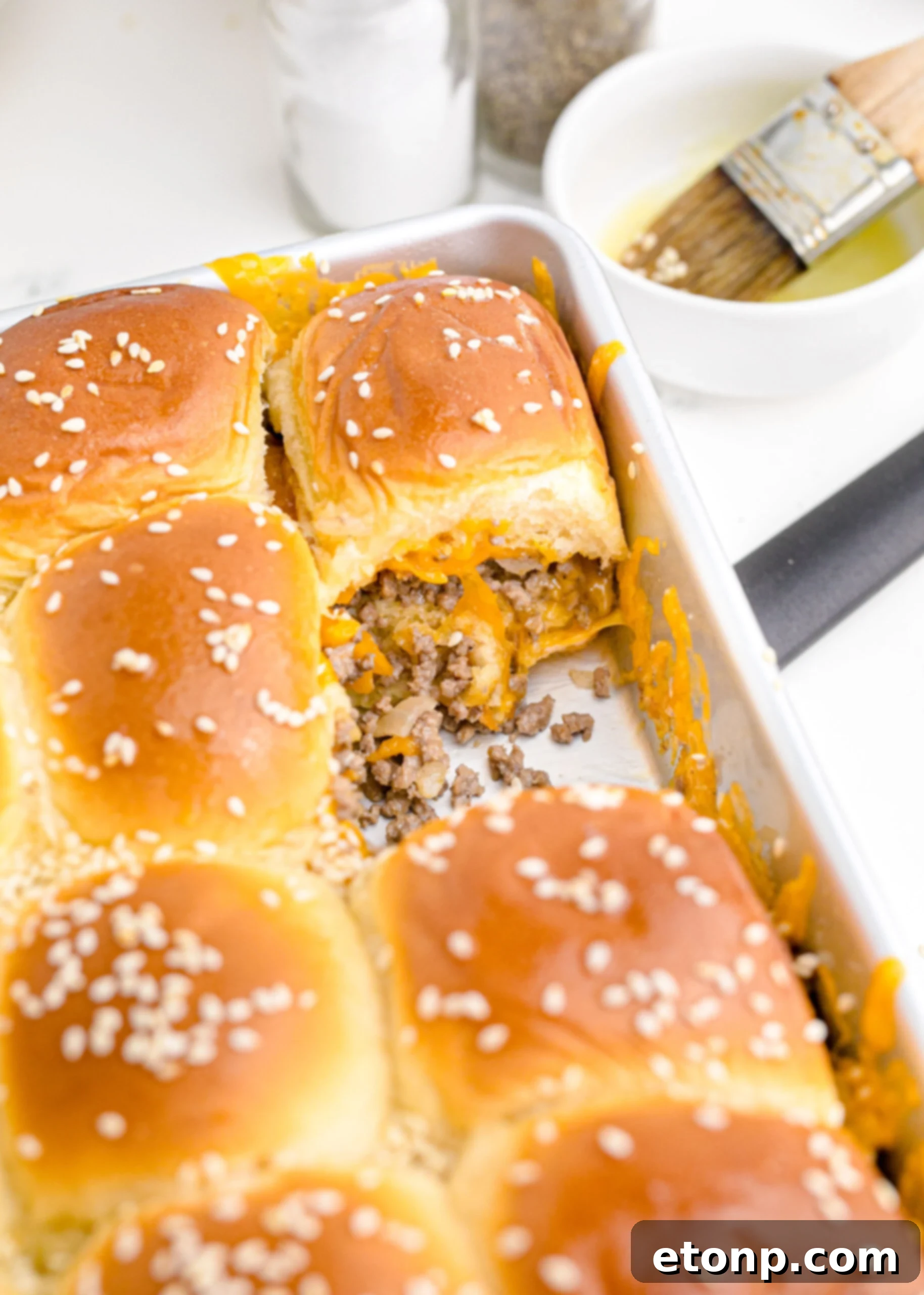 A baking pan filled to the brim with perfectly baked Classic Cheeseburger Sliders, with one happily missing, indicating their irresistible appeal and deliciousness.