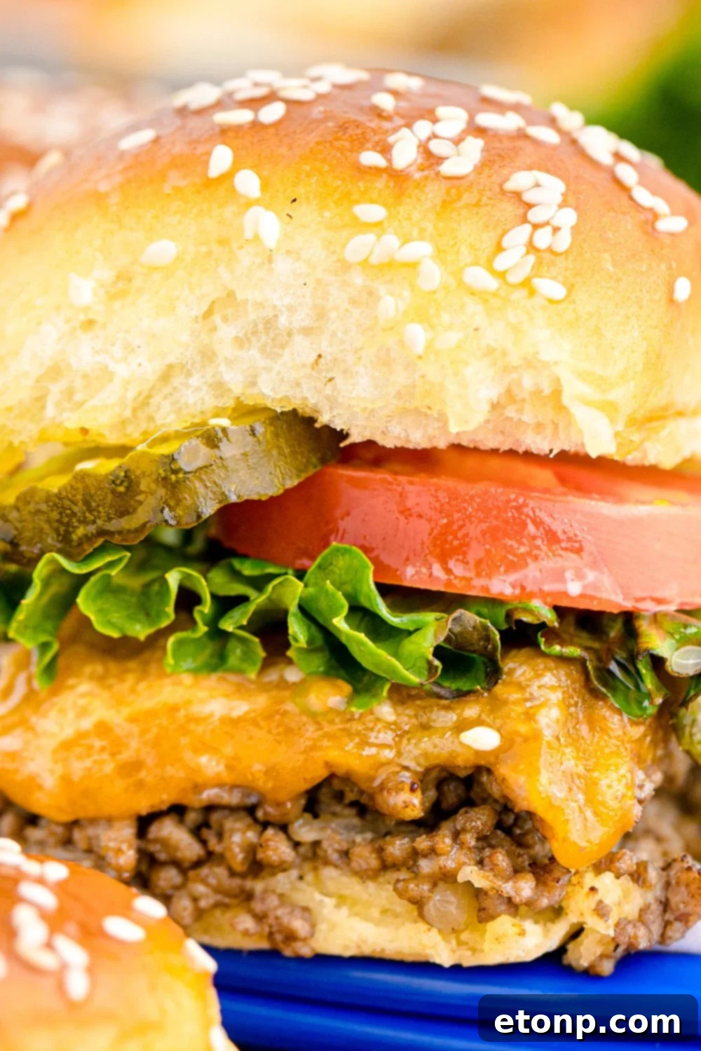 A mouth-watering close-up of a Classic Cheeseburger Slider, generously topped with a vibrant red tomato slice, fresh green lettuce, and a crisp pickle, showcasing its delectable layers and inviting appeal.
