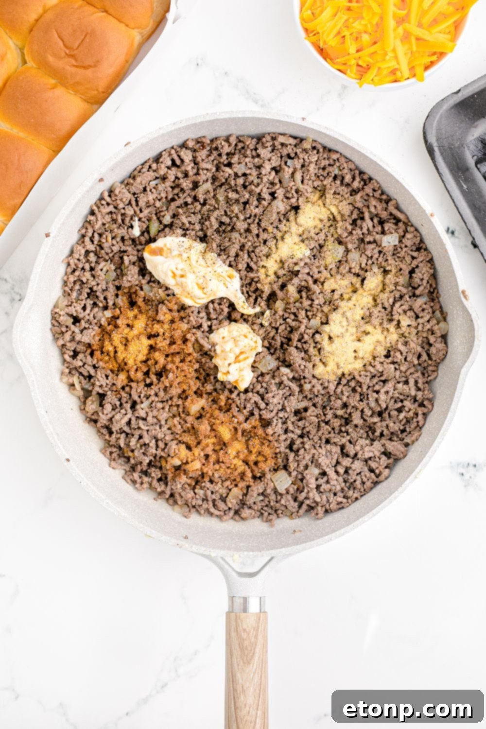 Perfectly cooked ground beef, still in the skillet, generously topped with a colorful array of spices and seasonings, ready to be mixed for the slider filling.