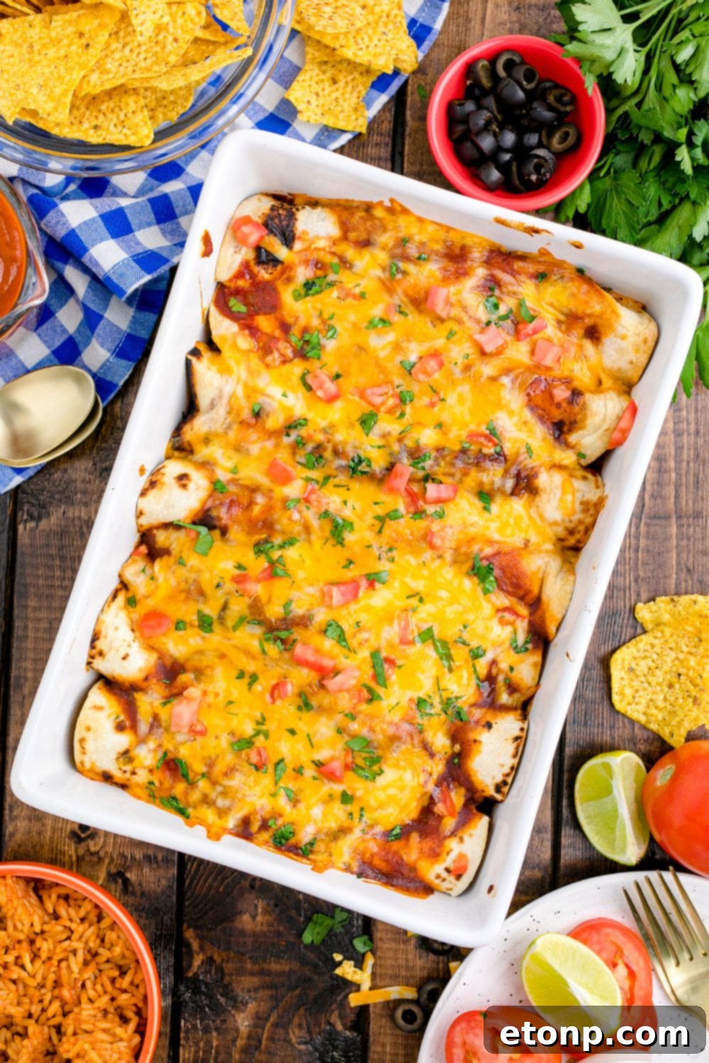 From Scratch Enchilada Perfection 12 overhead picture of a casserole dish full of enchiladas on table. Condiments and ingredients in bowls on table around the pan, highlighting a festive meal