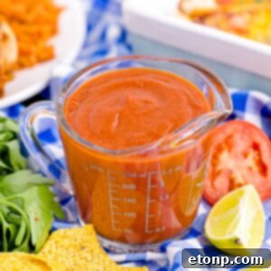 From Scratch Enchilada Perfection 17 Homemade Enchilada Sauce in a measuring cup on table with tomato, lemon wedge and more around container
