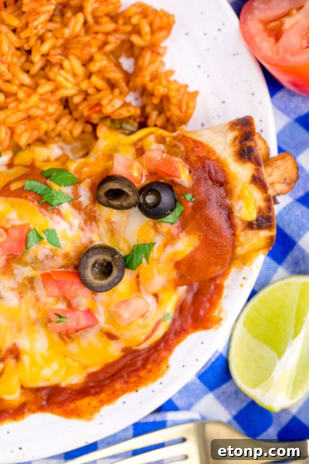 From Scratch Enchilada Perfection 3 close up of enchilada topped with cheese and a side of rice to the side on plate, generously coated with homemade red sauce