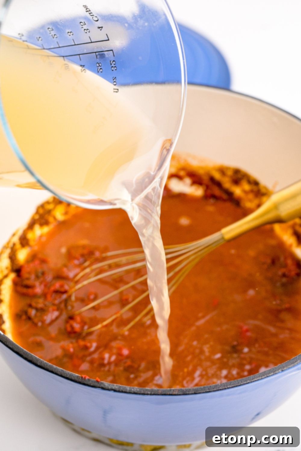 From Scratch Enchilada Perfection 8 Homemade Enchilada Sauce being made with stock being poured into pan with tomato mixture in it, creating the perfect consistency