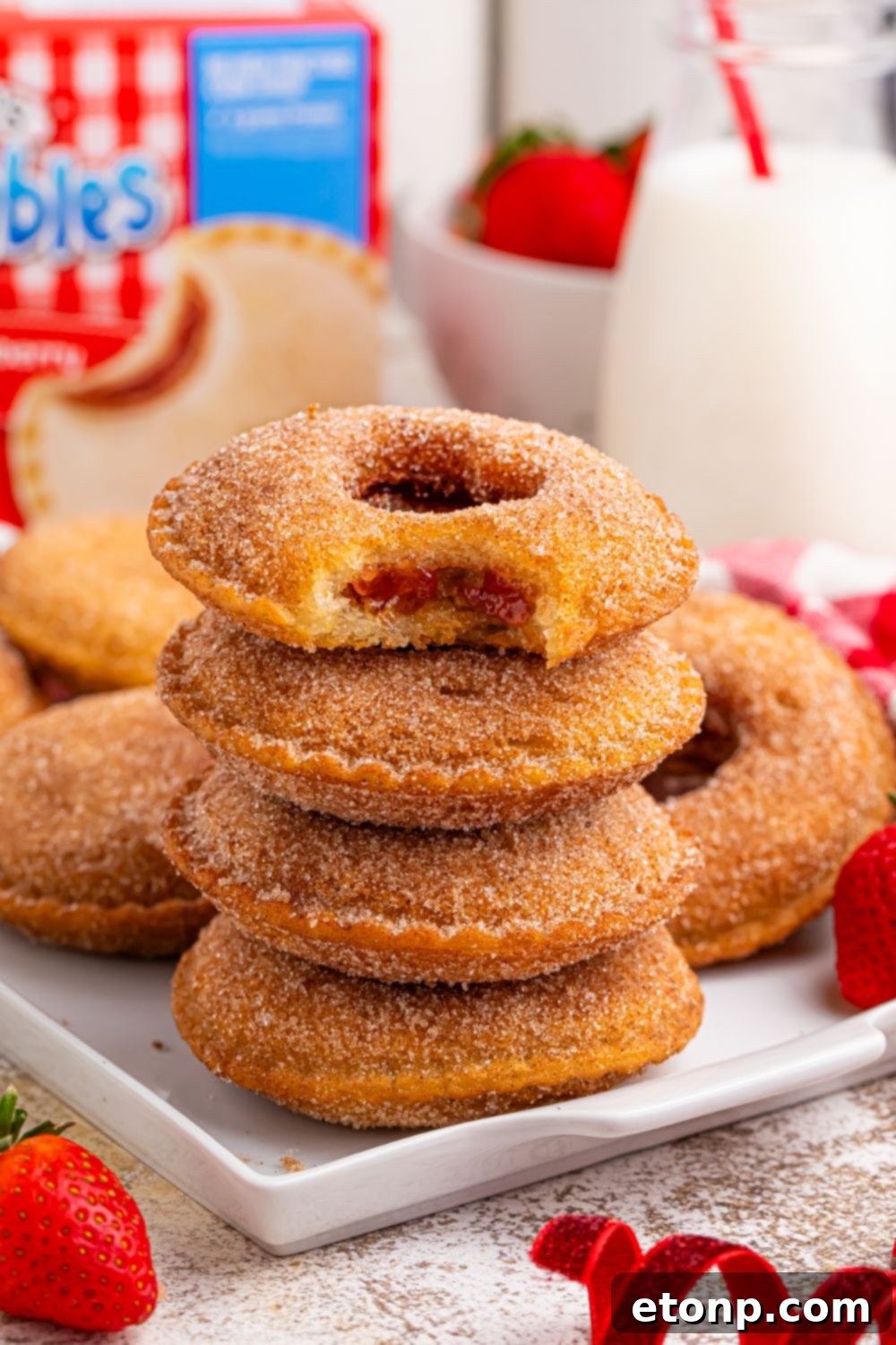 TikTok Fried Strawberry Uncrustables 11 Stack of fried Uncrustables on a plate, with more spread out on a tray behind, alongside a tall glass of milk and the Uncrustables box