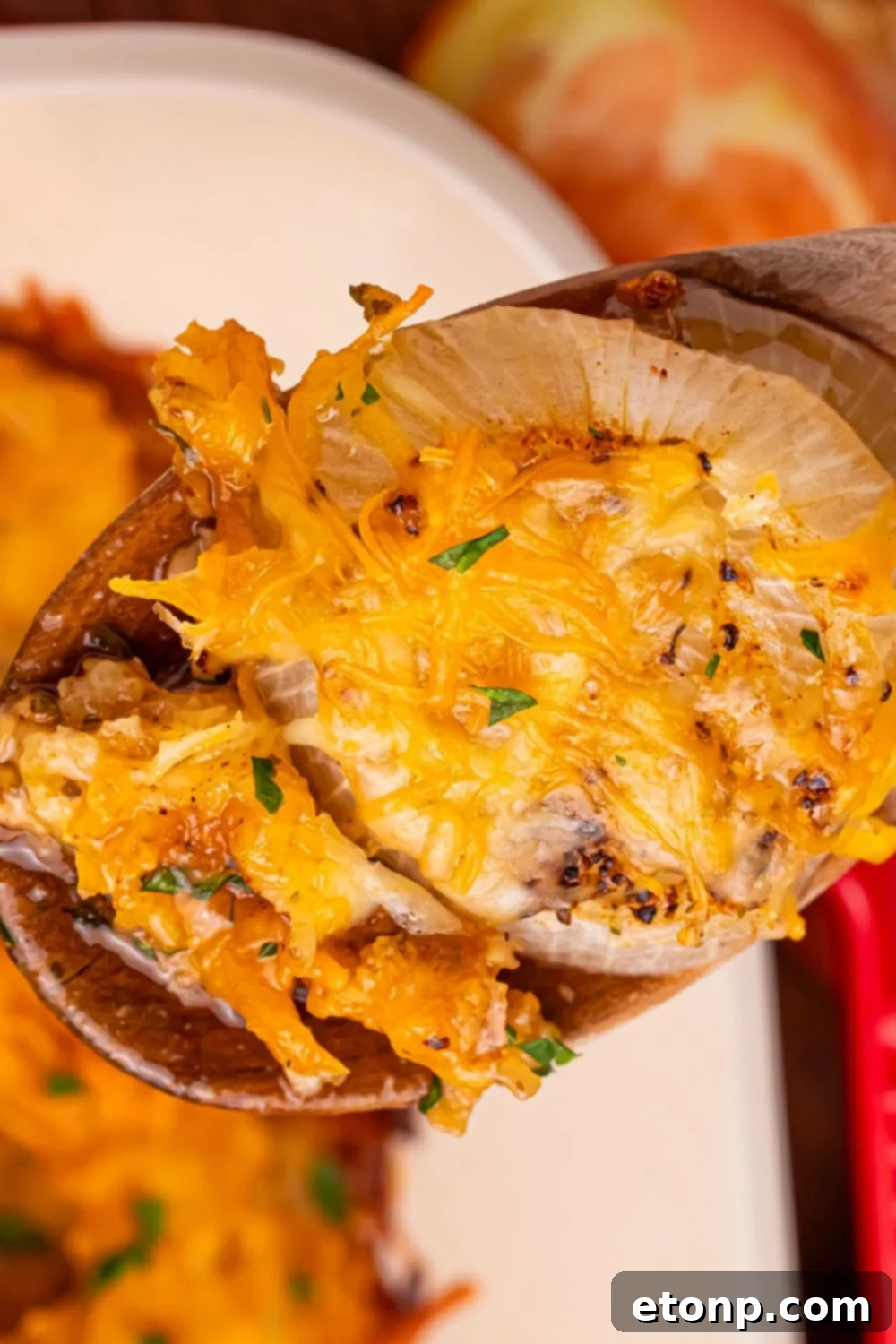 Cheesy Tennessee Onion Bake 14 A wooden spoon scooping out a portion of Cheesy Tennessee Onions from a baking dish, highlighting its texture.