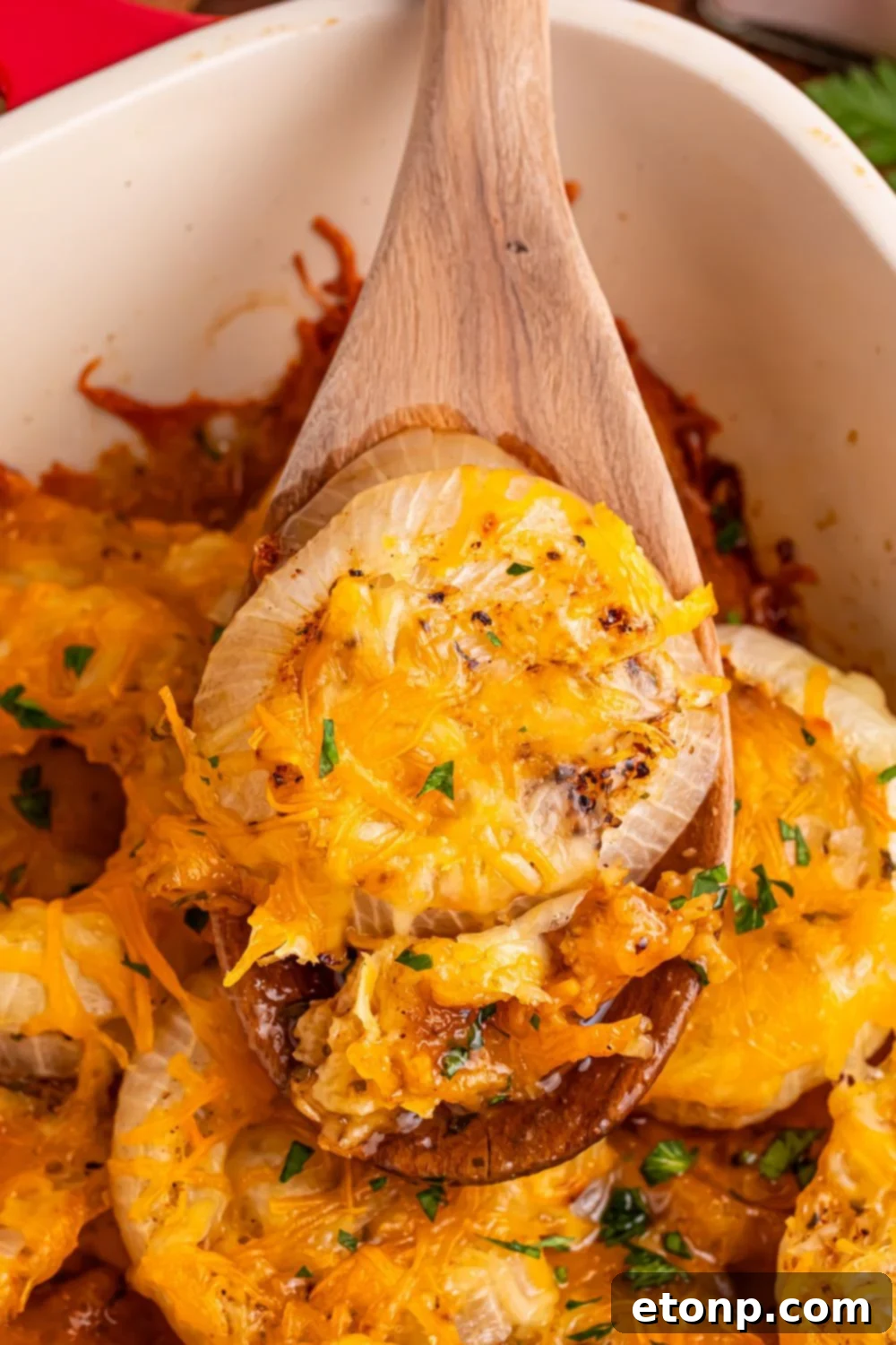 Cheesy Tennessee Onion Bake 3 Scooping baked Cheesy Tennessee Onions from a casserole pan with a serving spoon, showing the gooey cheese.