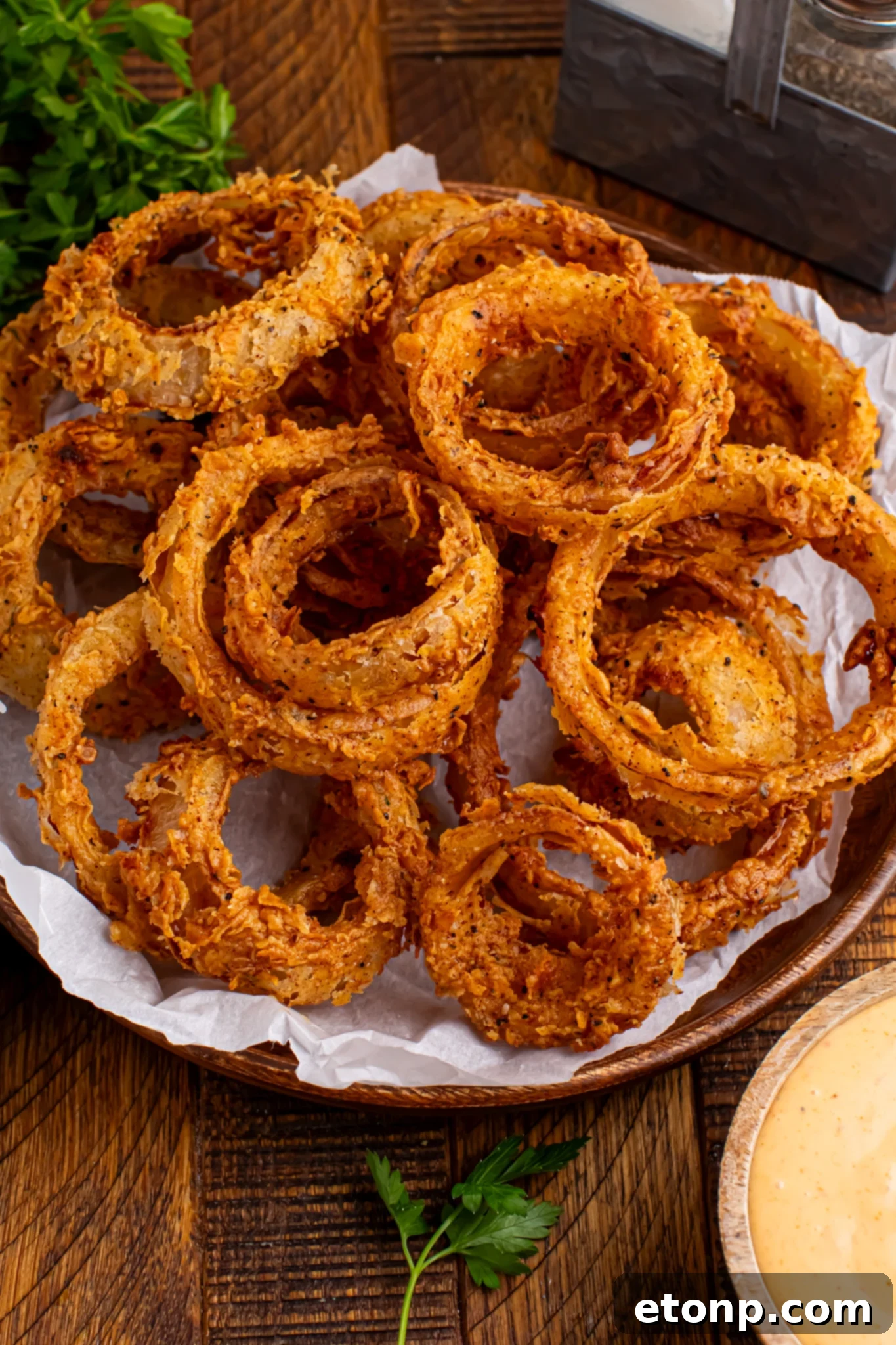 Golden Crispy Homemade Onion Rings 2 Homemade Deep Fried Onion Rings piled into a plate on table with a dipping sauce in a bowl in front