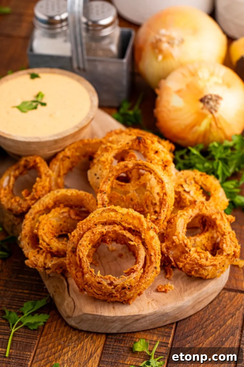 Golden Crispy Homemade Onion Rings 11 Homemade Deep Fried Onion Rings on a cutting board with whole onions behind it on table