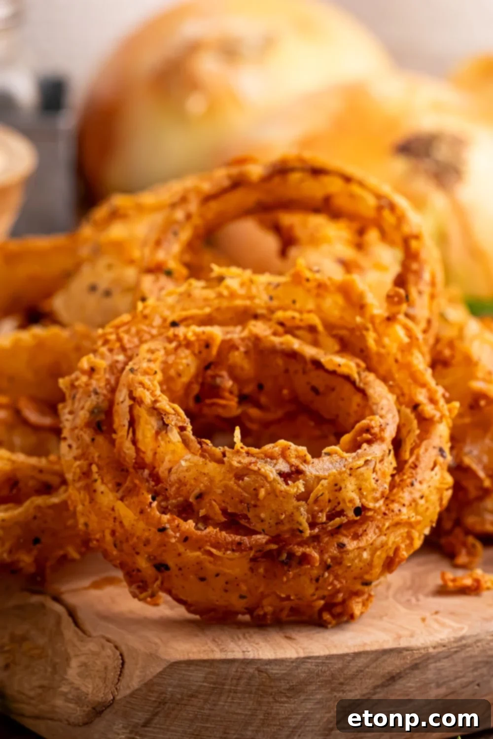 Golden Crispy Homemade Onion Rings 12 close up look of Homemade Deep Fried Onion Rings on a wooden tray with yellow onions behind it
