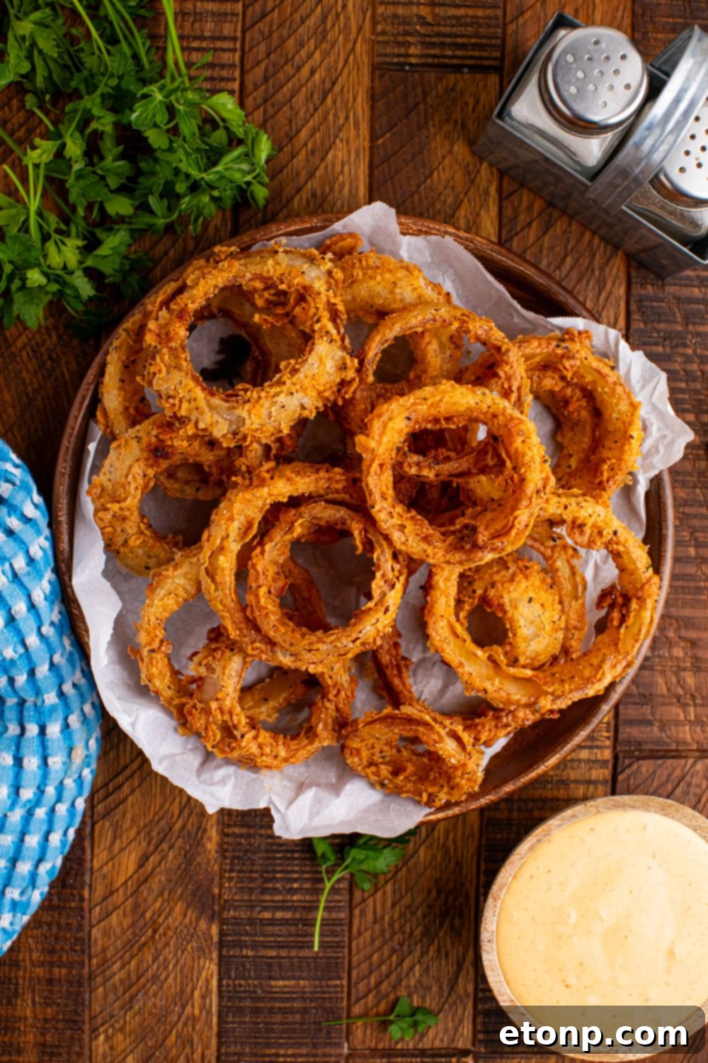 Golden Crispy Homemade Onion Rings 14 overhead look of table with Homemade Deep Fried Onion Rings in a bowl and sauce, salt, and pepper on table as well