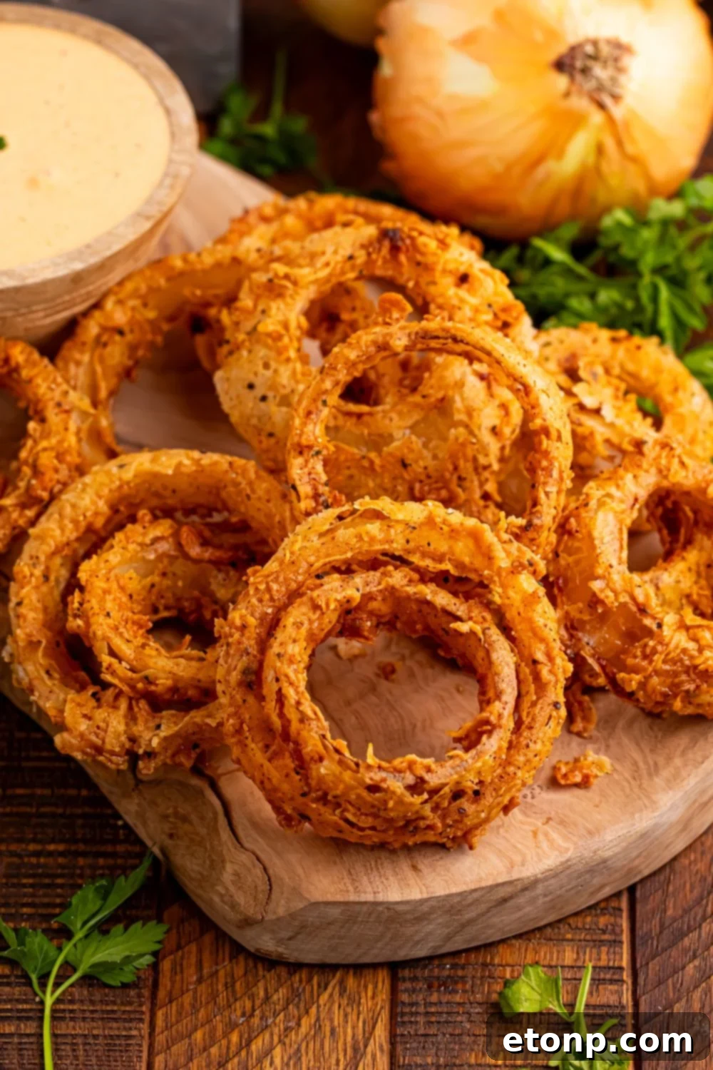 Golden Crispy Homemade Onion Rings 15 Homemade Deep Fried Onion Rings on a cutting tray with parsley in front and side of tray, with some sauce in a small bowl for dipping