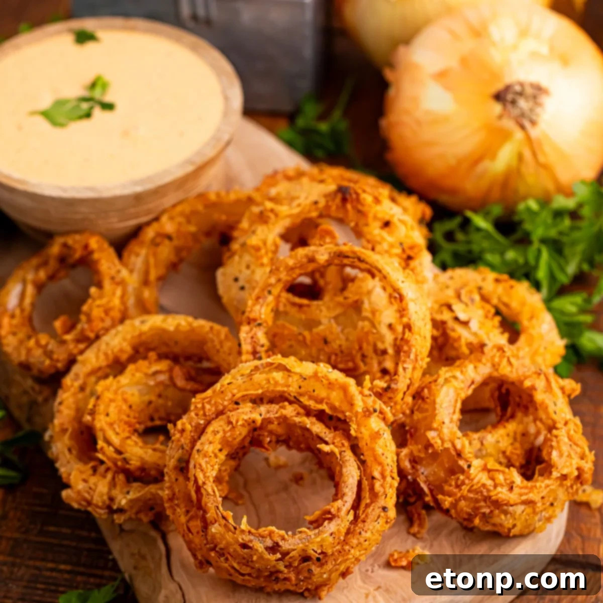 Golden Crispy Homemade Onion Rings 3 Homemade Deep Fried Onion Rings placed on a cutting board with a dipping sauce in bowl and onions on table