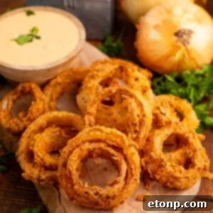 Golden Crispy Homemade Onion Rings 24 Homemade Deep Fried Onion Rings placed on a cutting board with a dipping sauce in bowl and onions on table