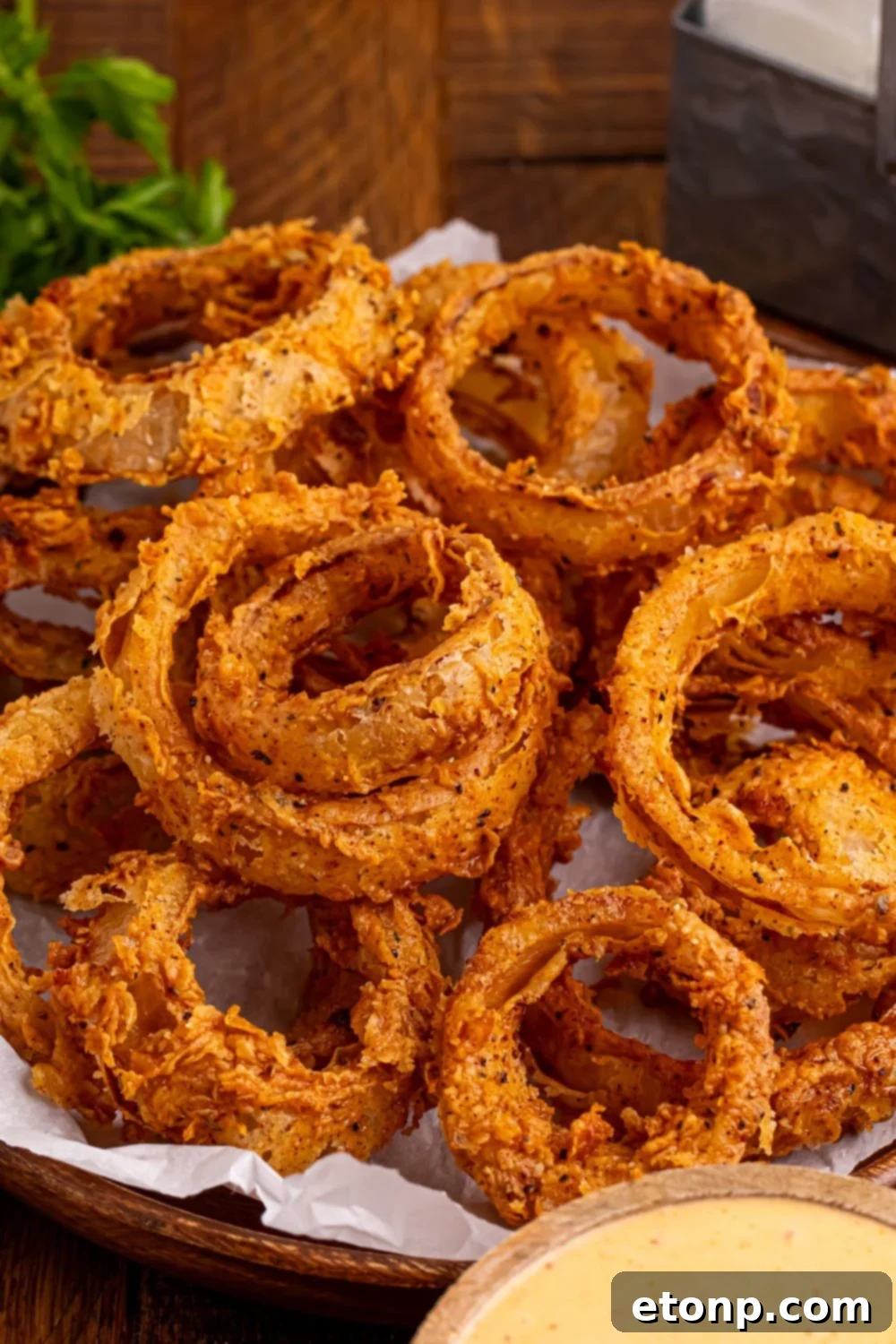 Golden Crispy Homemade Onion Rings 6 Homemade Deep Fried Onion Rings piled into a plate on table with a dipping sauce in a bowl in front