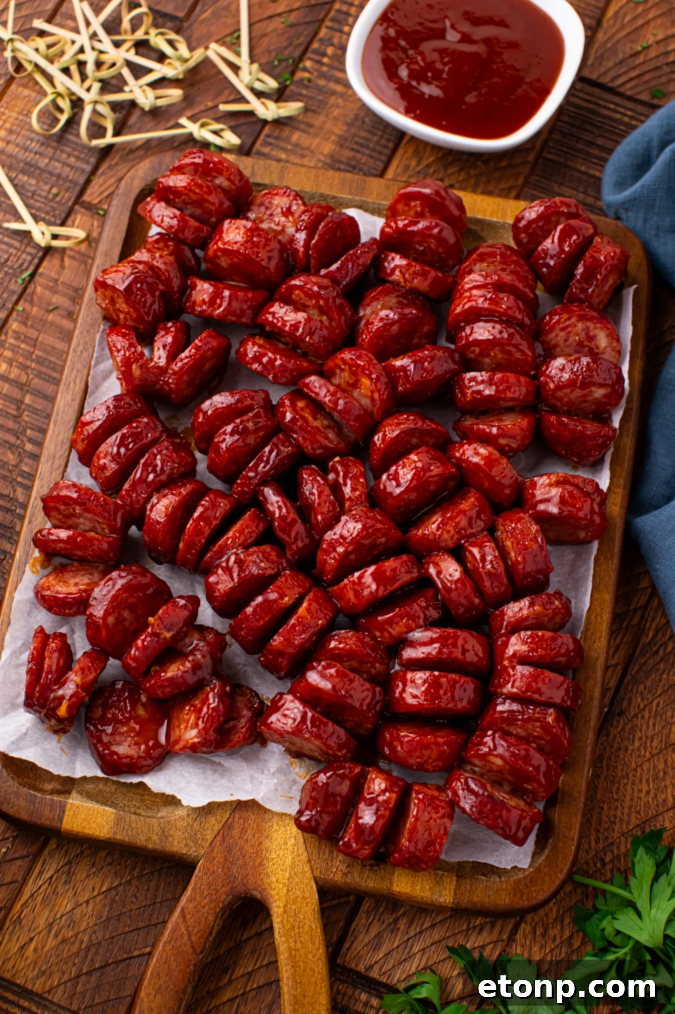 BBQ Hasselback Smoked Sausages on a wooden cutting board with a side of BBQ sauce 