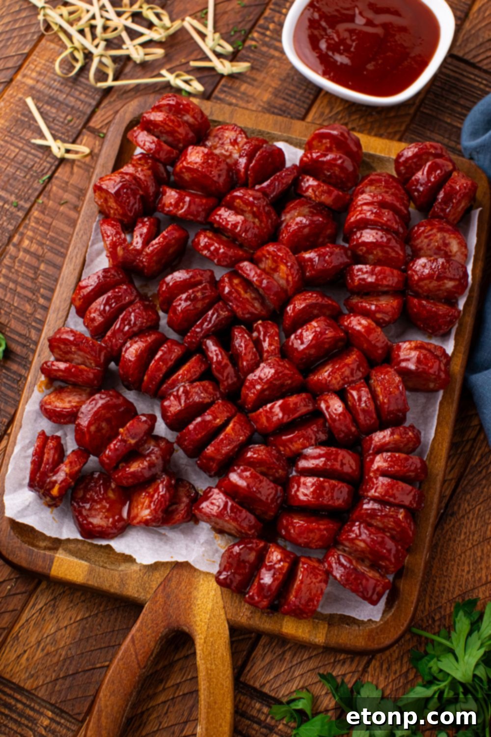 BBQ Hasselback Smoked Sausages on a cutting board with a bowl of sauce 