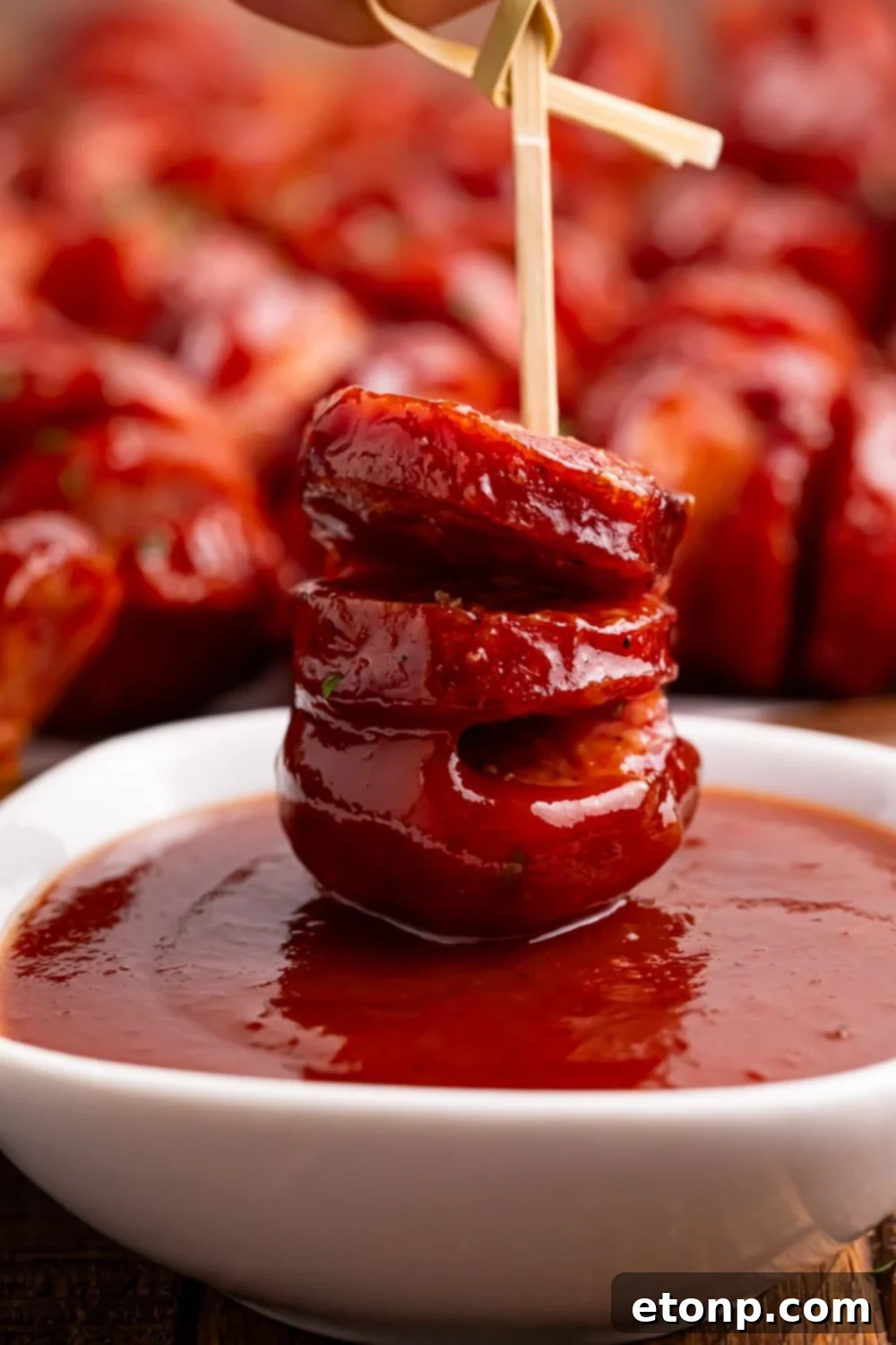BBQ Hasselback Smoked Sausages dipped in sauce in a bowl 