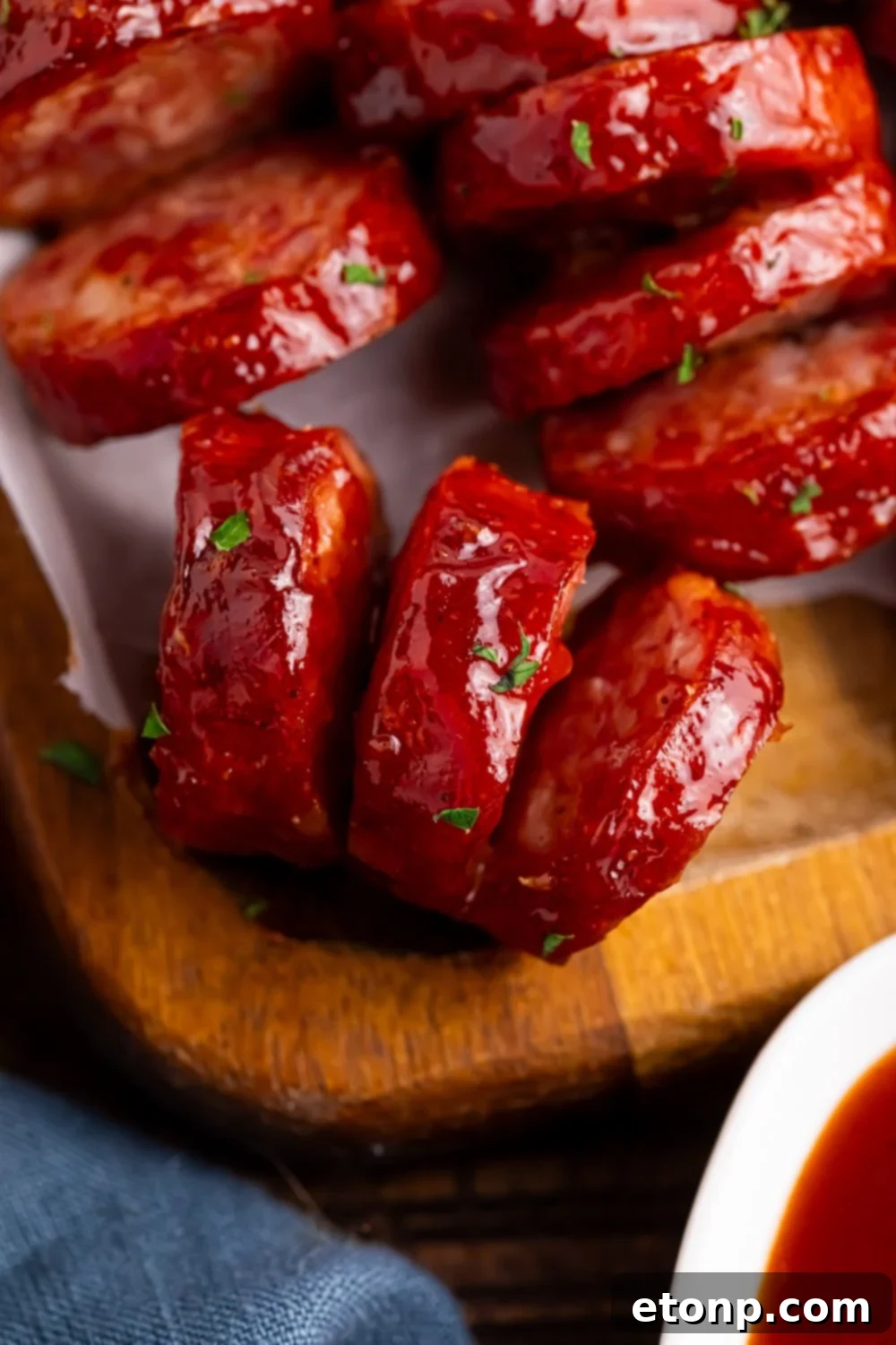 close up of BBQ Hasselback Smoked Sausages on a wooden cutting board with a side of sauce 
