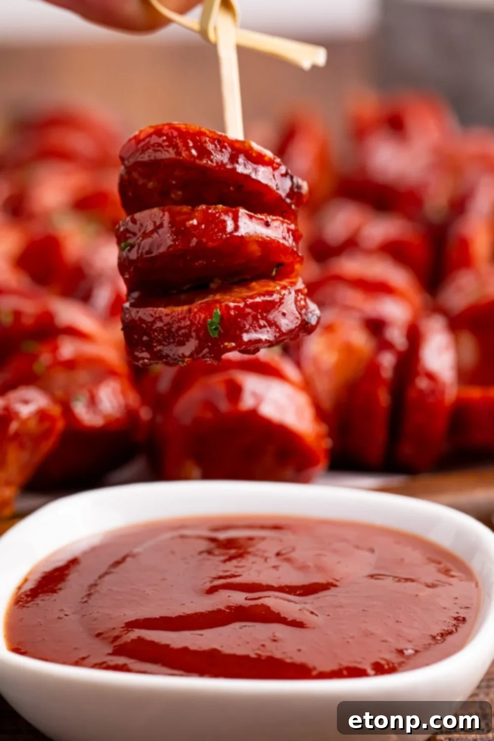 BBQ Hasselback Smoked Sausages being held above a bowl of sauce on table 