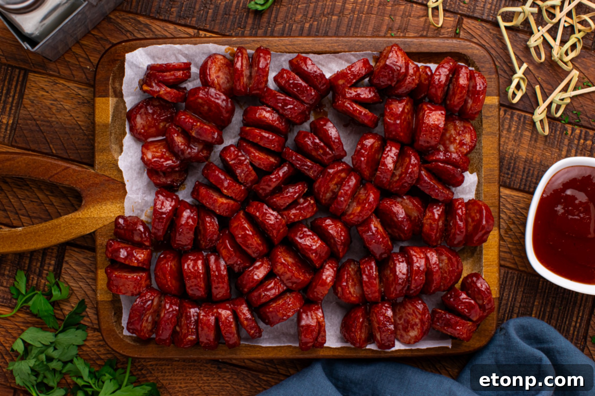 overhead view of BBQ Hasselback Smoked Sausages spread out on a dark wood cutting board