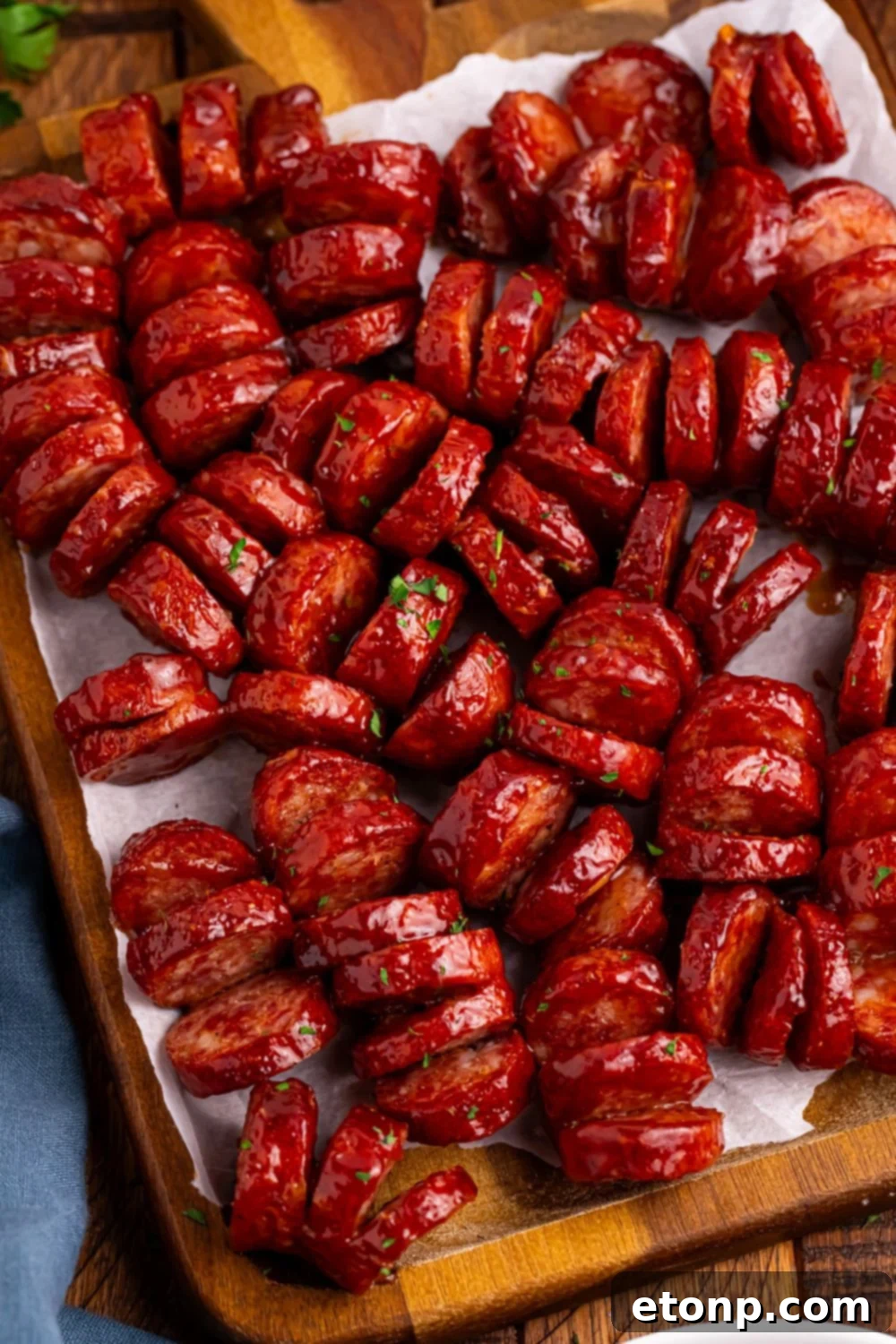 BBQ Hasselback Smoked Sausages on cutting board with parchment paper under the meat 