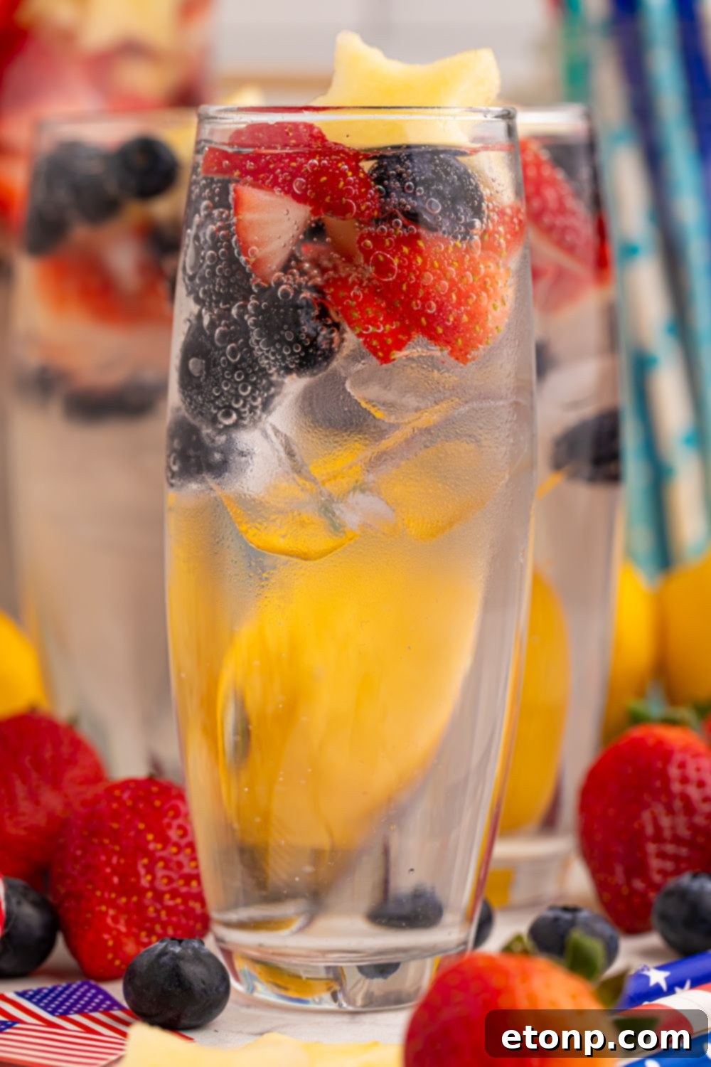 Liberty Lemon Sparkle 14 Patriotic Sparkling Lemonade in glasses topped with fruit in each glass. Fruit is scattered on table
