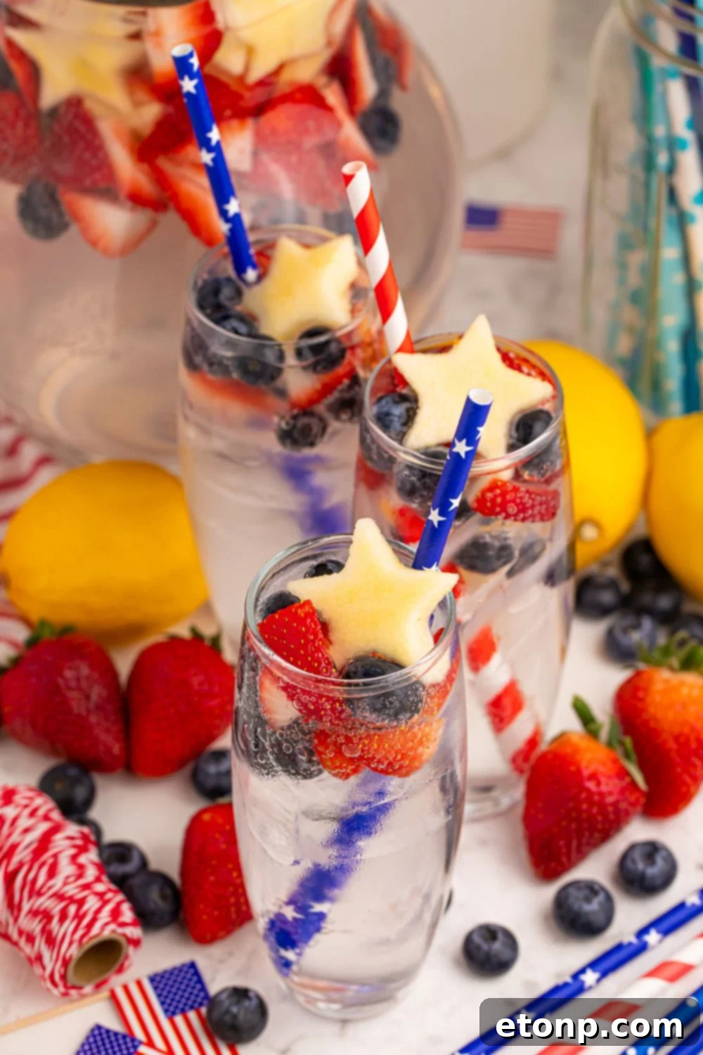 Liberty Lemon Sparkle 15 Patriotic Sparkling Lemonades in glasses on table with lemons, strawberries, and blueberries around the table