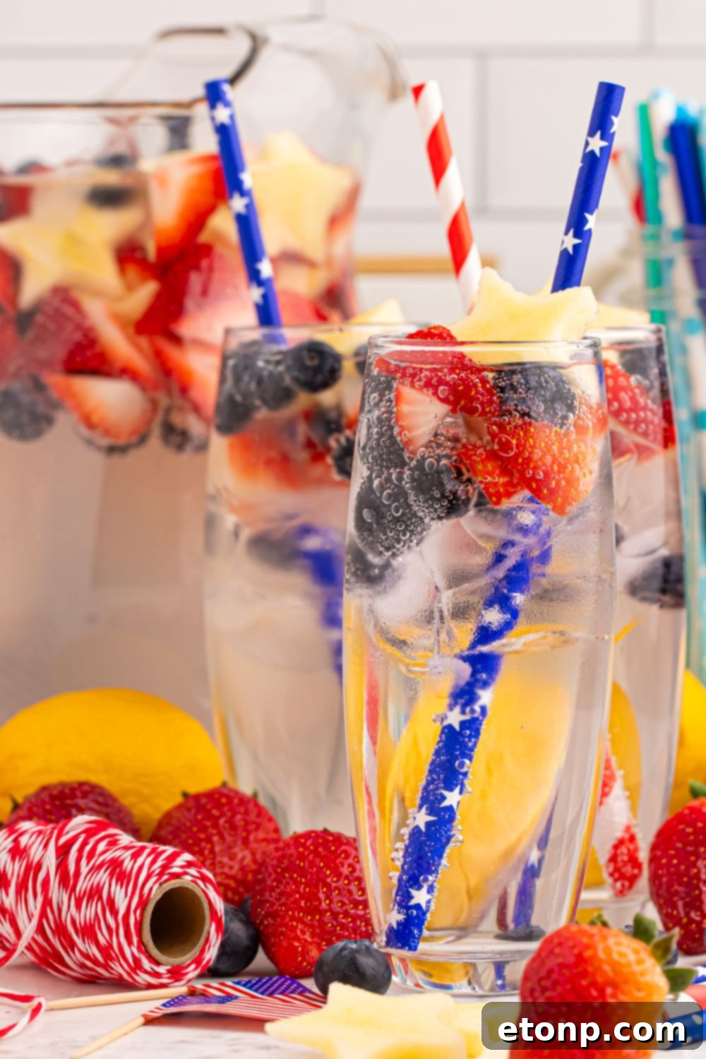 Liberty Lemon Sparkle 19 sparkling lemonade in glasses with a pitcher full of lemonade behind it on table there is red and white string on table to add a pop of color