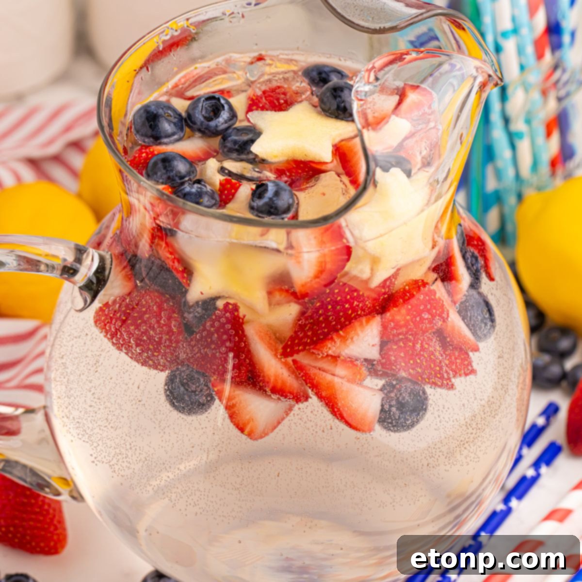 Liberty Lemon Sparkle 3 Patriotic Sparkling Lemonade in a pitcher with red white and blue fruit and ice in pitcher sitting on table