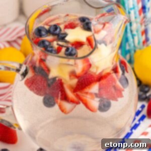 Liberty Lemon Sparkle 26 Patriotic Sparkling Lemonade in a pitcher with red white and blue fruit and ice in pitcher sitting on table