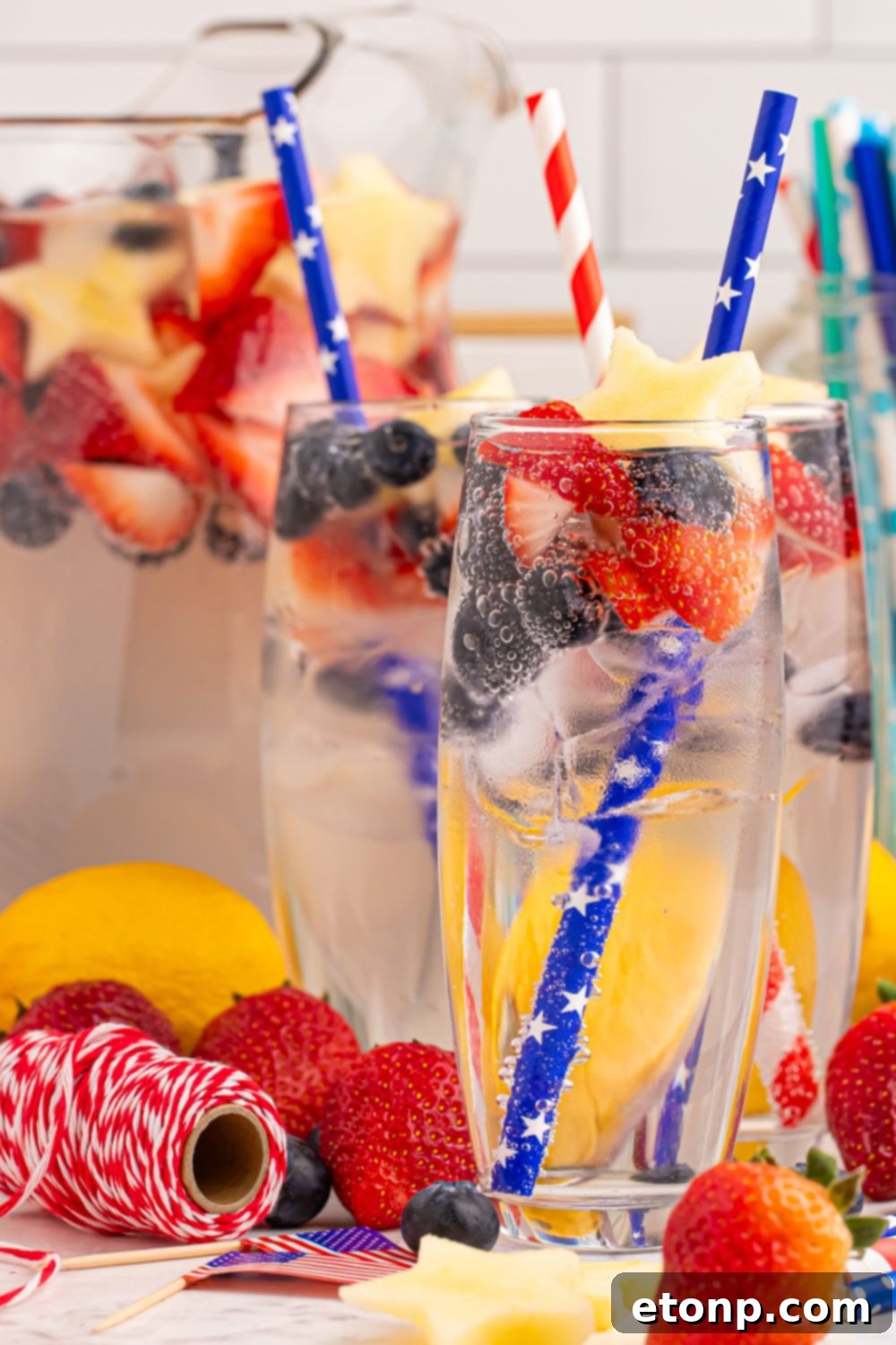 Liberty Lemon Sparkle 7 Patriotic Sparkling Lemonade in glasses and pitcher full of lemonade. All glasses are garnished with fruit