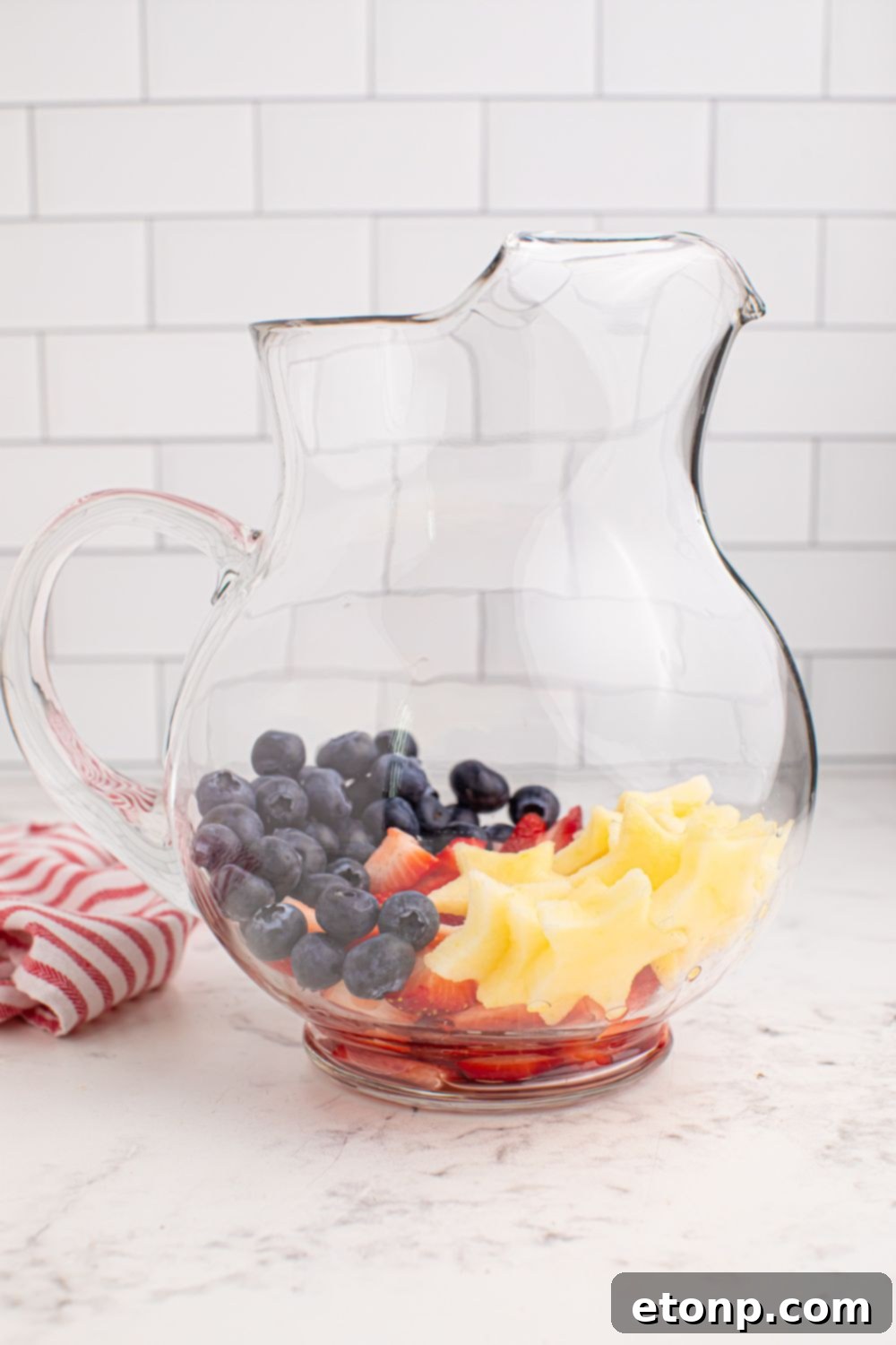 Liberty Lemon Sparkle 10 pitcher full of fruit sitting on table with a red and white towel to the side