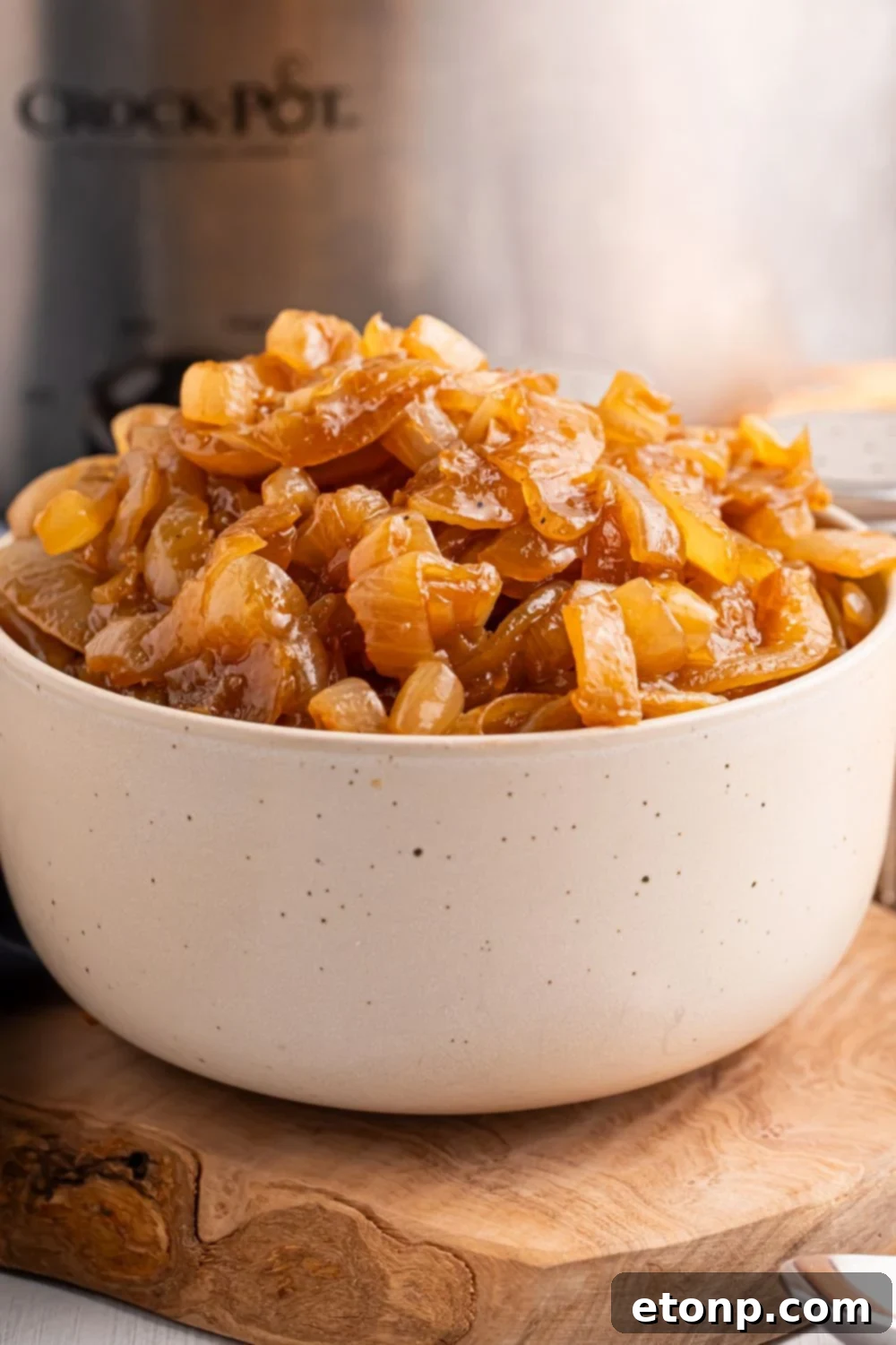 CrockPot Caramelized Onions in a white bowl on table with a CrockPot behind it on table 