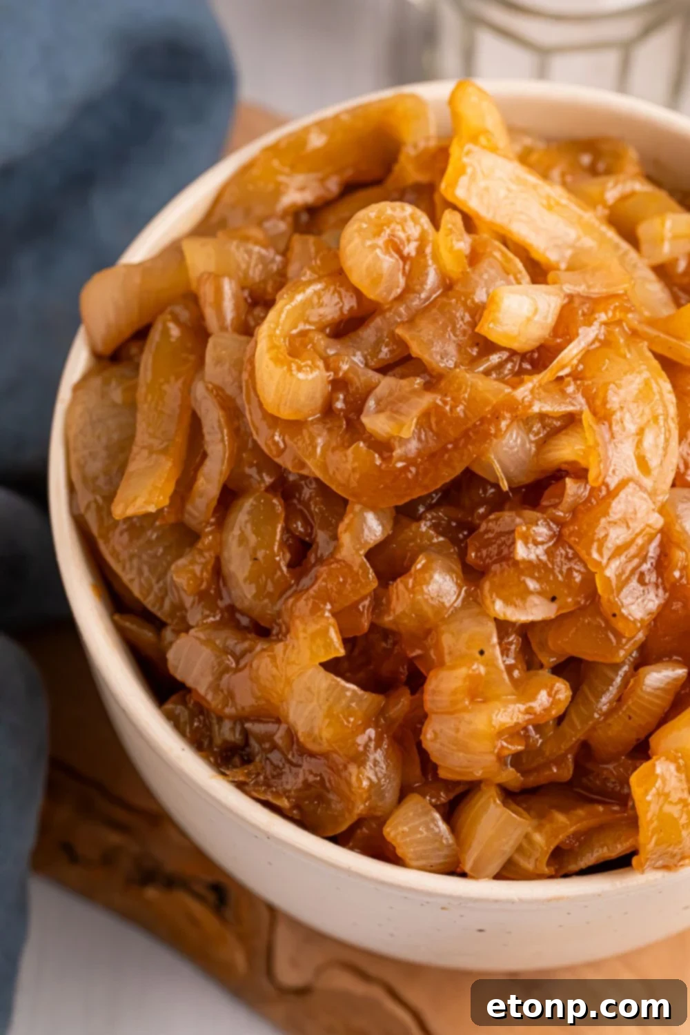 CrockPot Caramelized Onions in a white bowl on table with a blue towel to side of it 