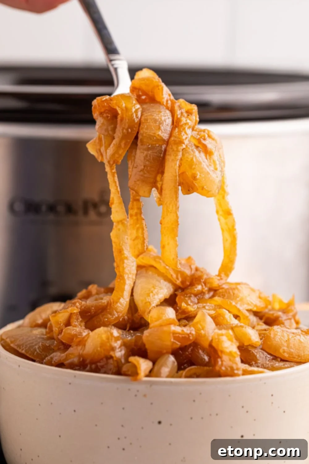 CrockPot Caramelized Onions and a bowl in front of CrockPot with a spoon lifting up some of the onions 